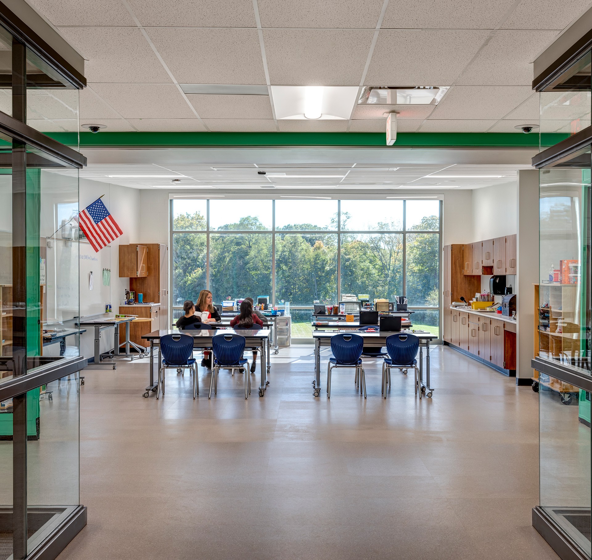 Bright Modern Classroom with Students and Large Window View Bright, modern classroom with large windows, desks, chairs, and a small group of students.