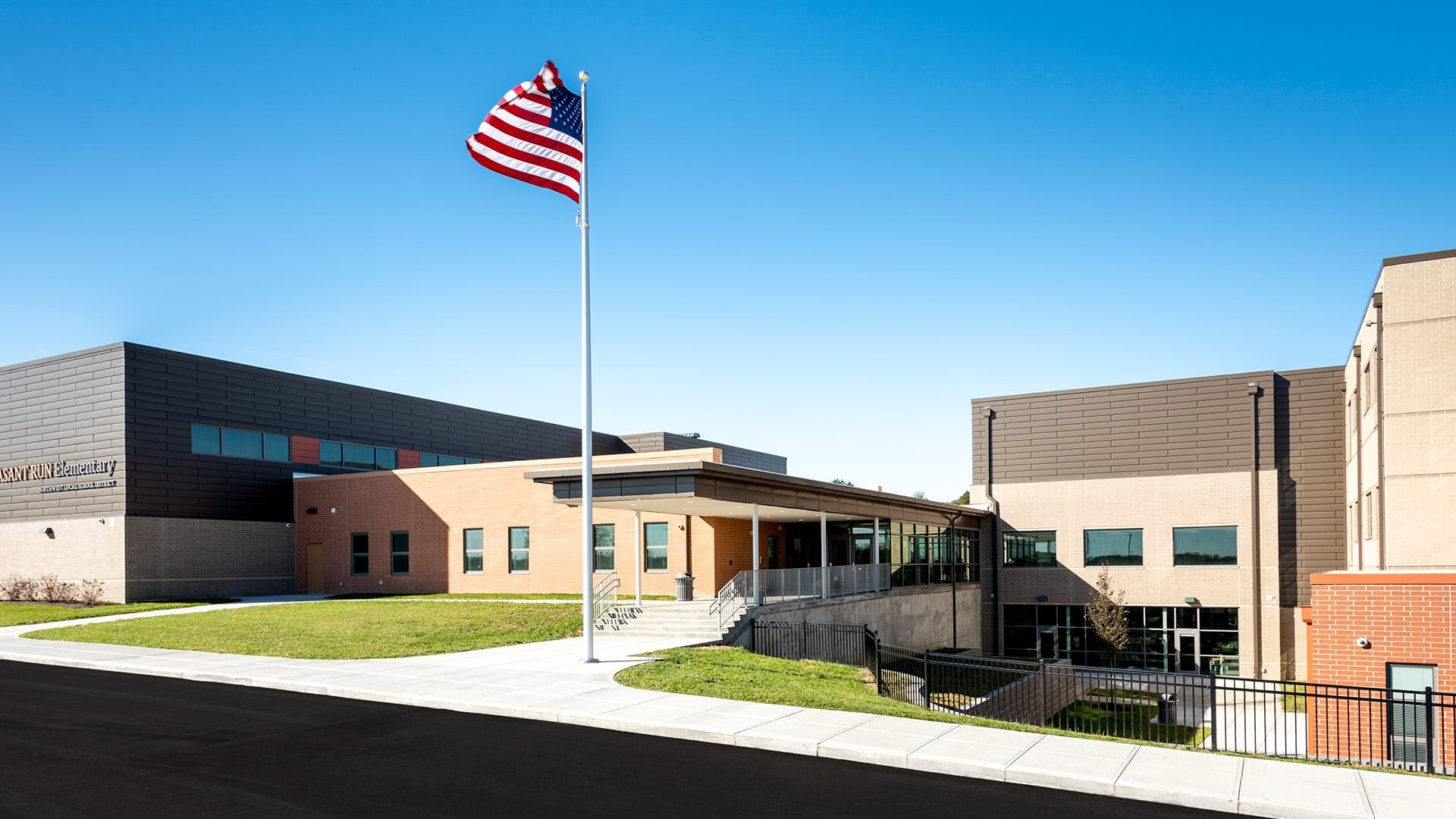 Modern school building with American flag under clear blue sky and paved sidewalk.