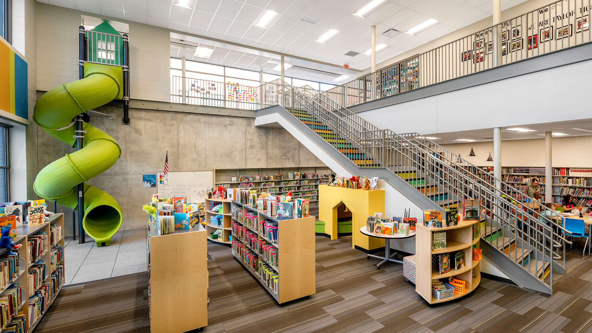 Modern library interior with bookshelves, a green slide, and a staircase.