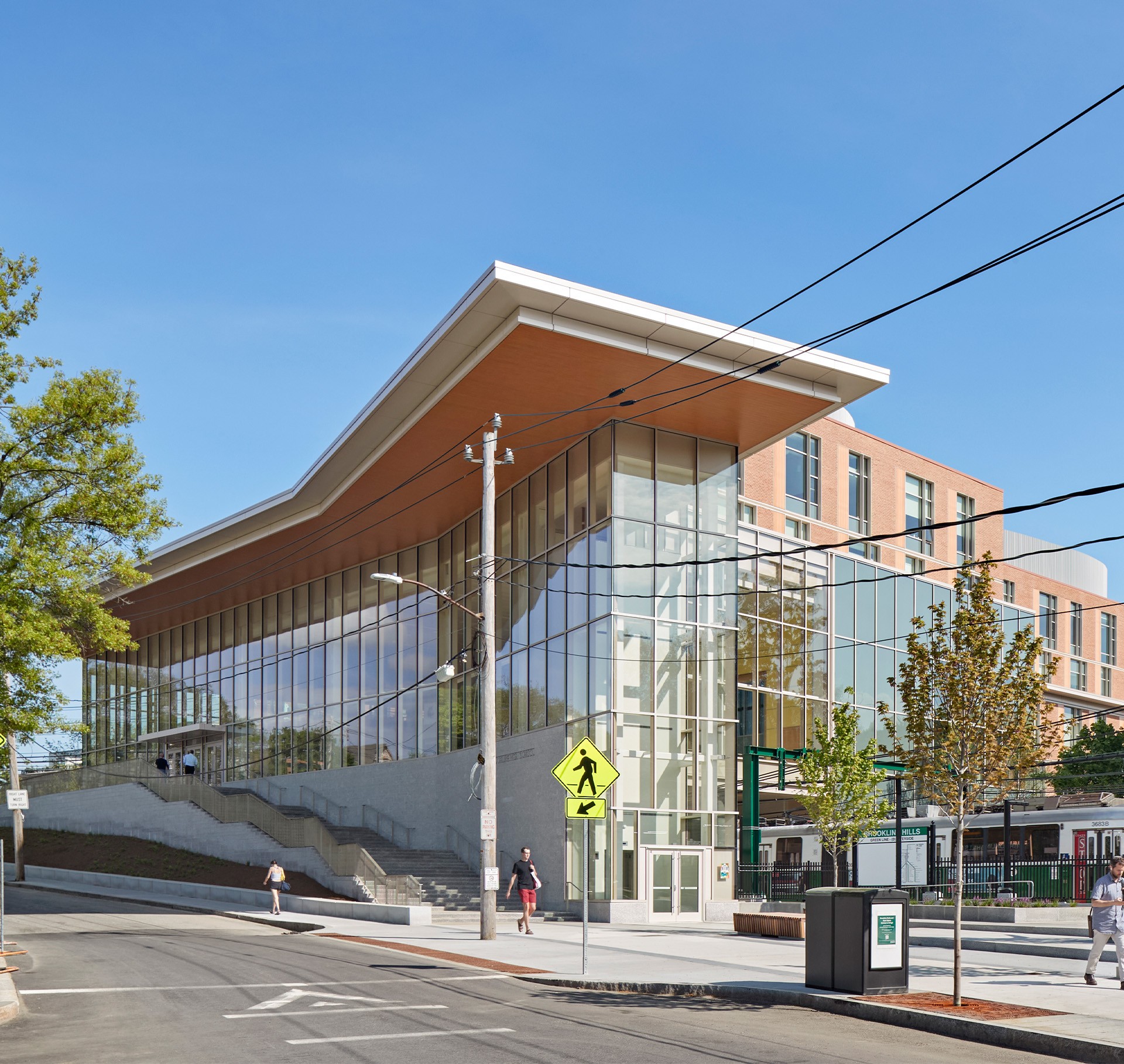 Modern Urban Library Building with Glass Facade and Trees Modern glass building with a slanted roof beside a street and pedestrian crossing sign.
