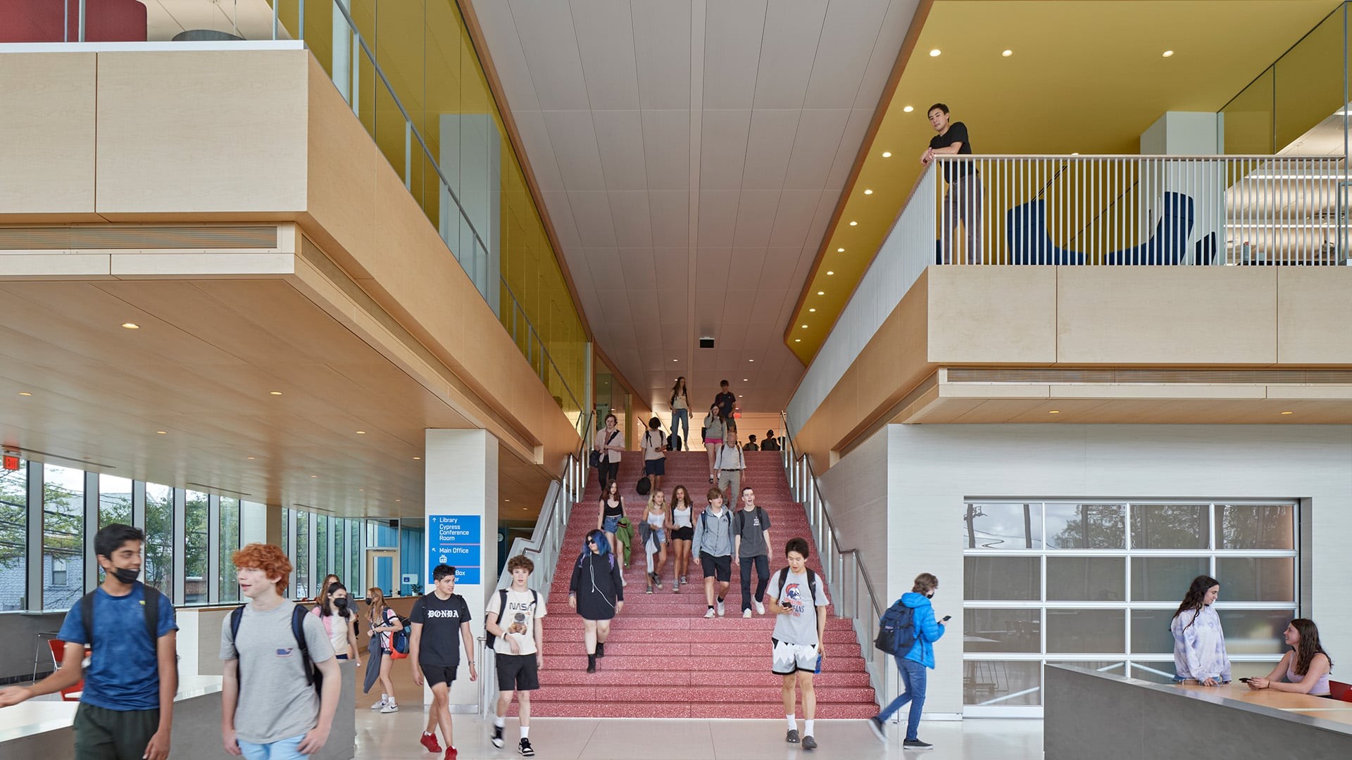 Students walking and socializing on wide indoor stairs in a modern school building.