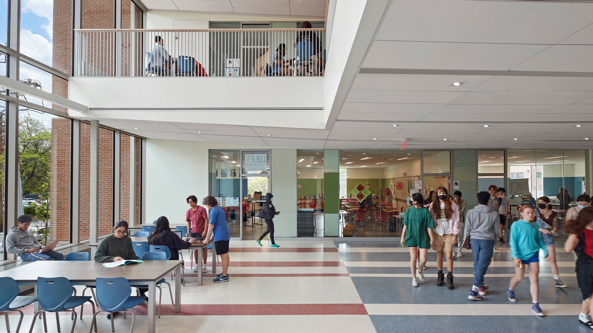 Students gather and study in a bright, modern school hallway with large windows.