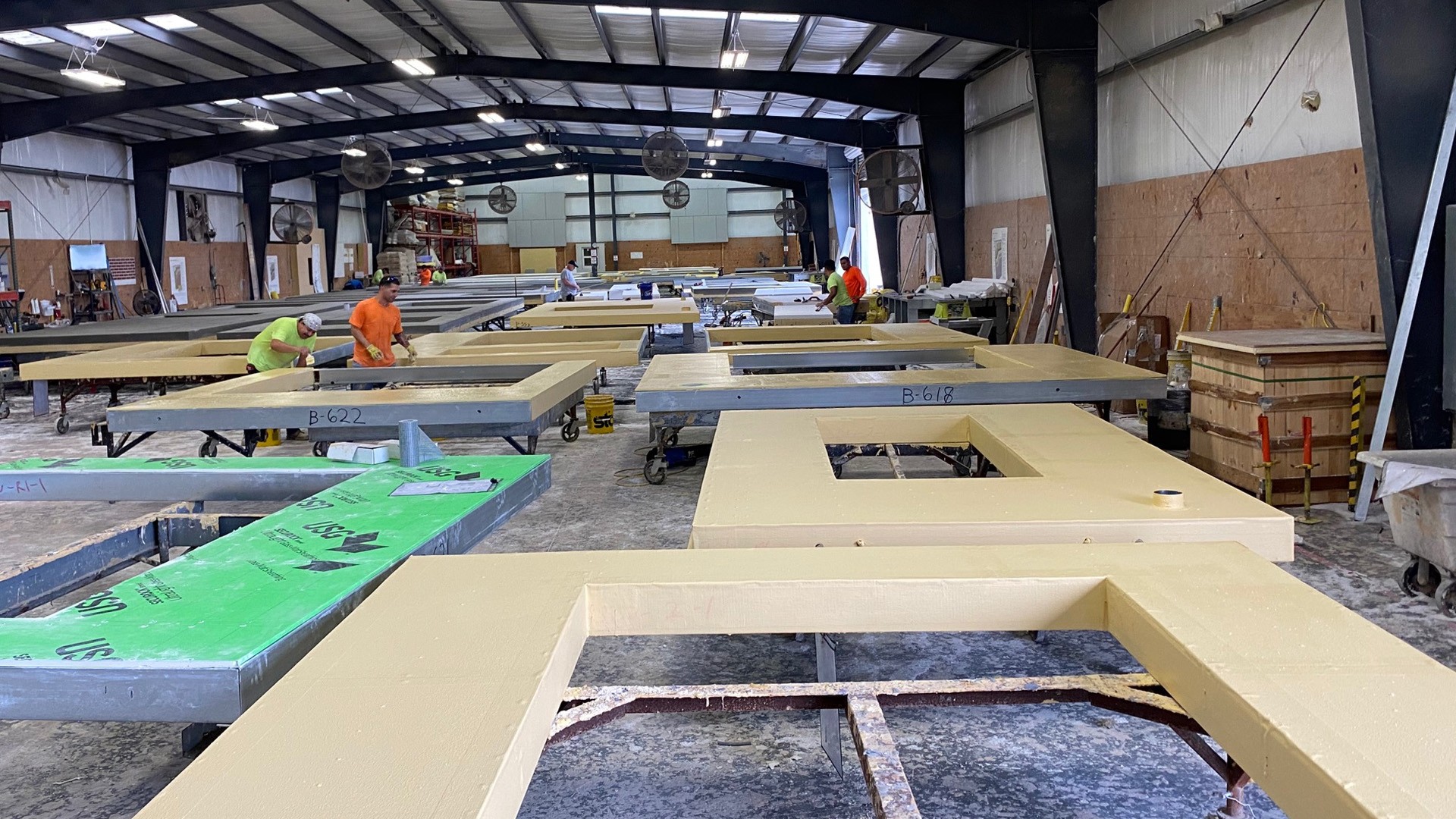 Factory workers assembling large construction panels indoors Workers assemble large insulated wall panels in a spacious factory workshop.