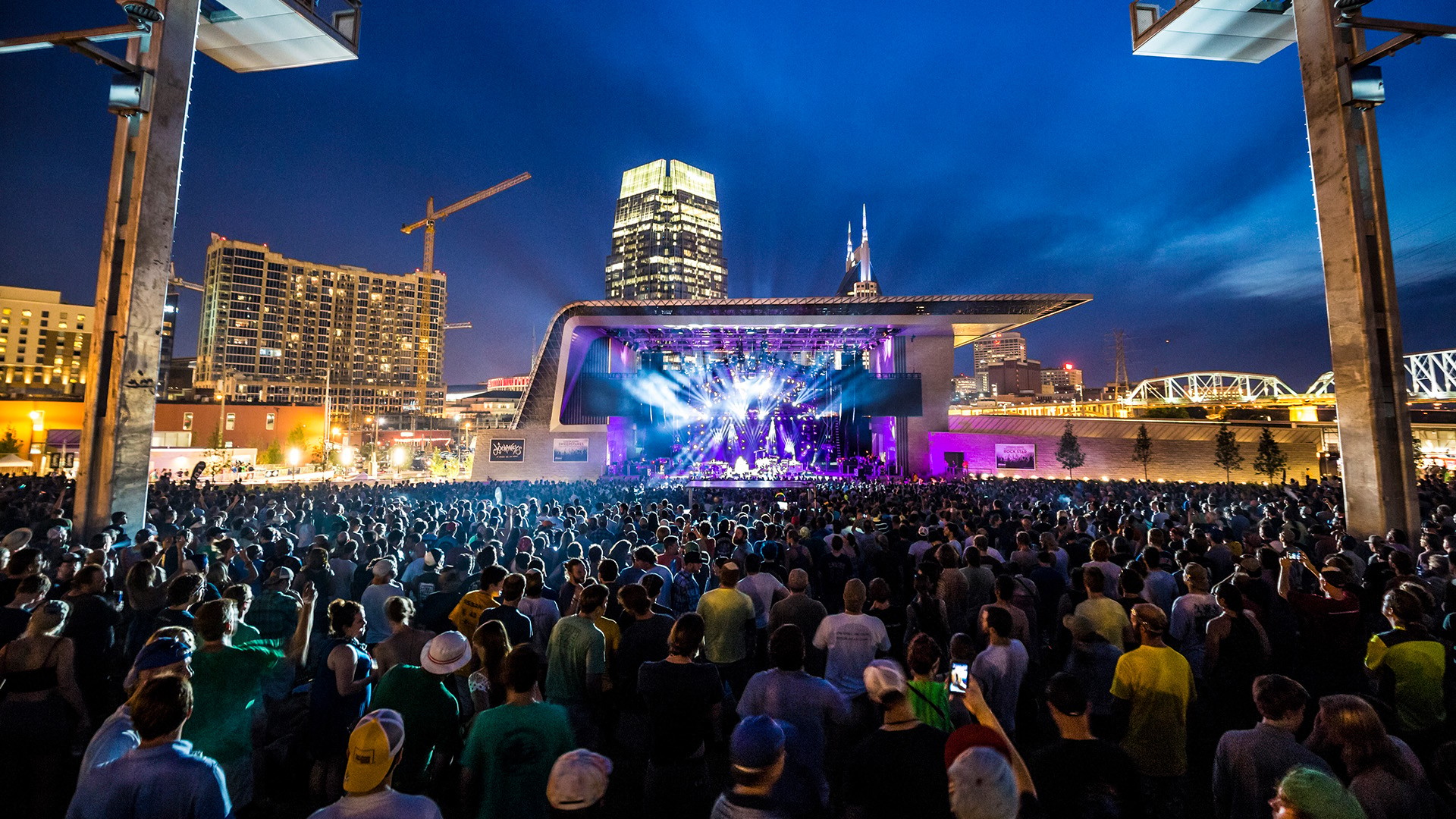 Outdoor Night Concert with Large Crowd and City Skyline Large crowd enjoying a vibrant outdoor concert at night in an urban amphitheater.