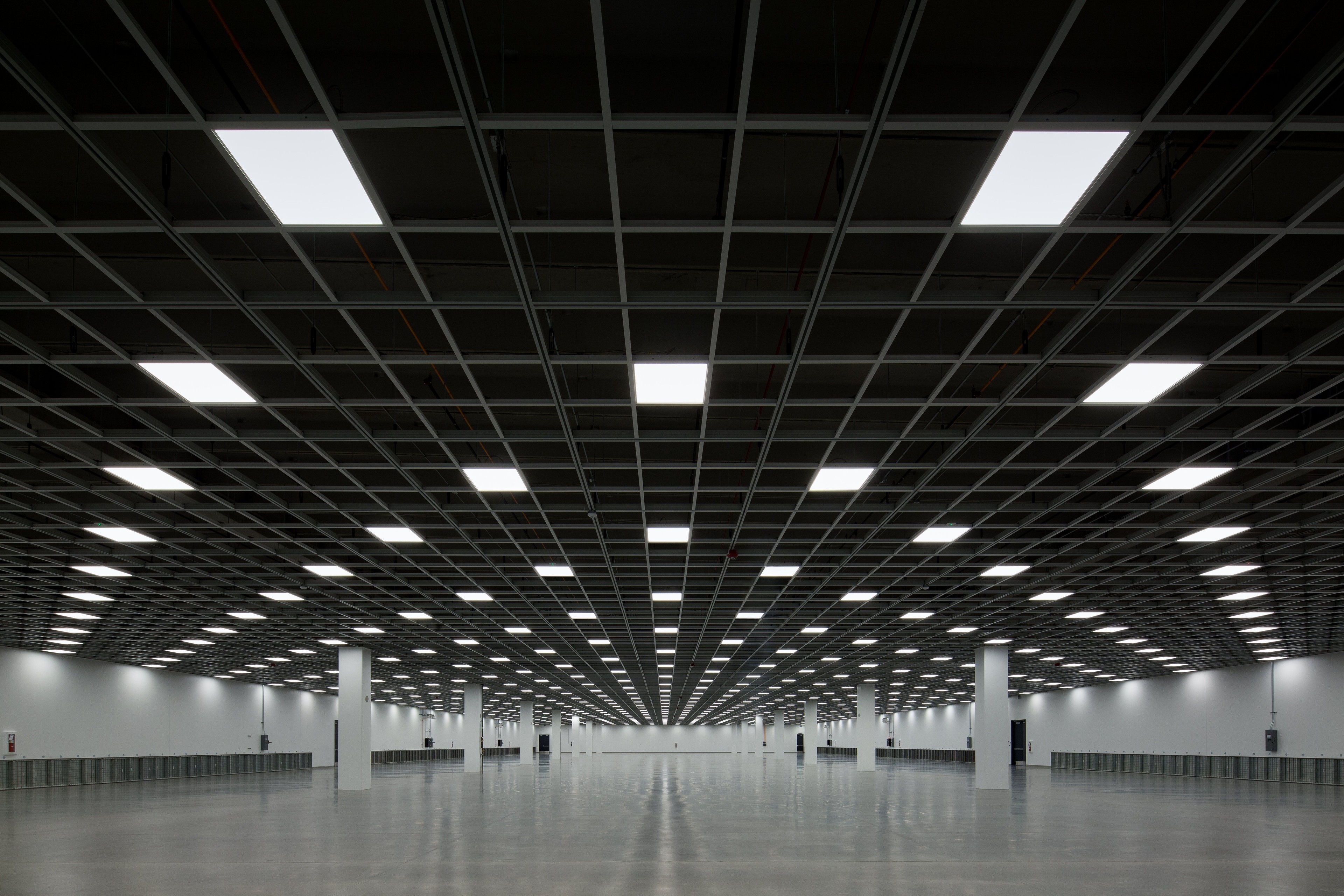 Data center server room with black server racks and white tiled floor under bright lights.