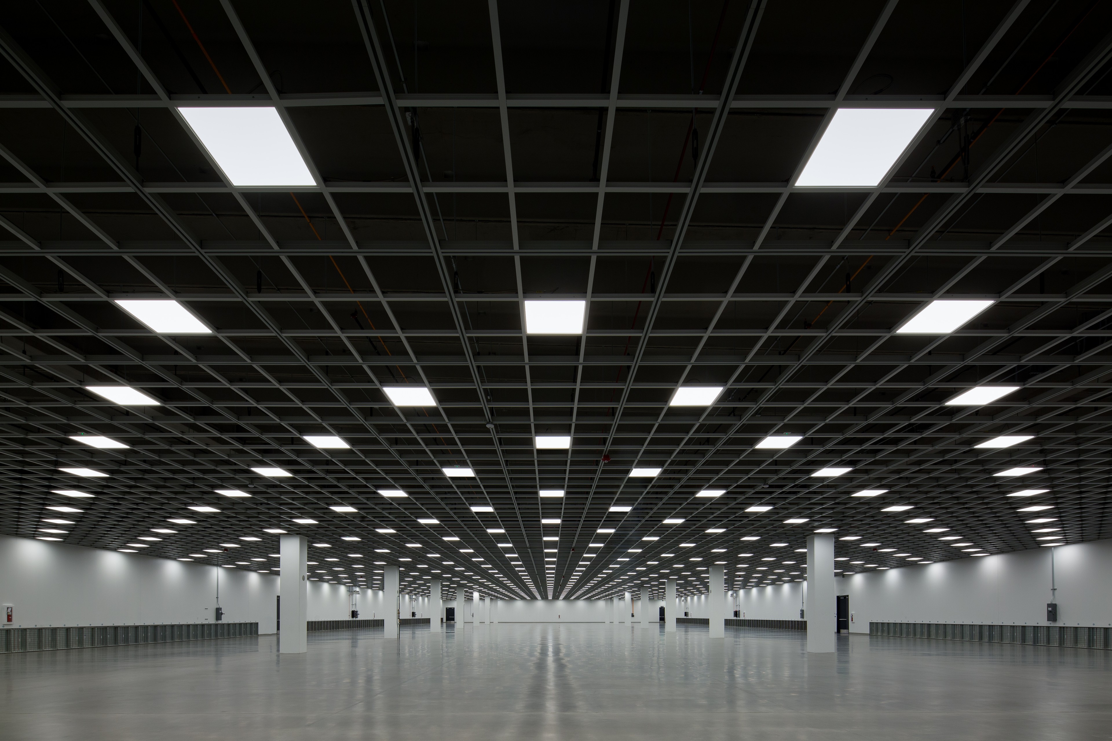 Data center server room with black server racks and white tiled floor under bright lights.