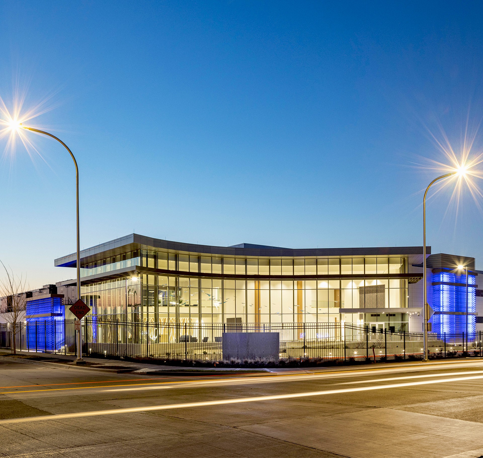 Modern Glass Building Illuminated at Dusk with Streetlights Modern glass building illuminated at dusk with streetlights and clear sky background.