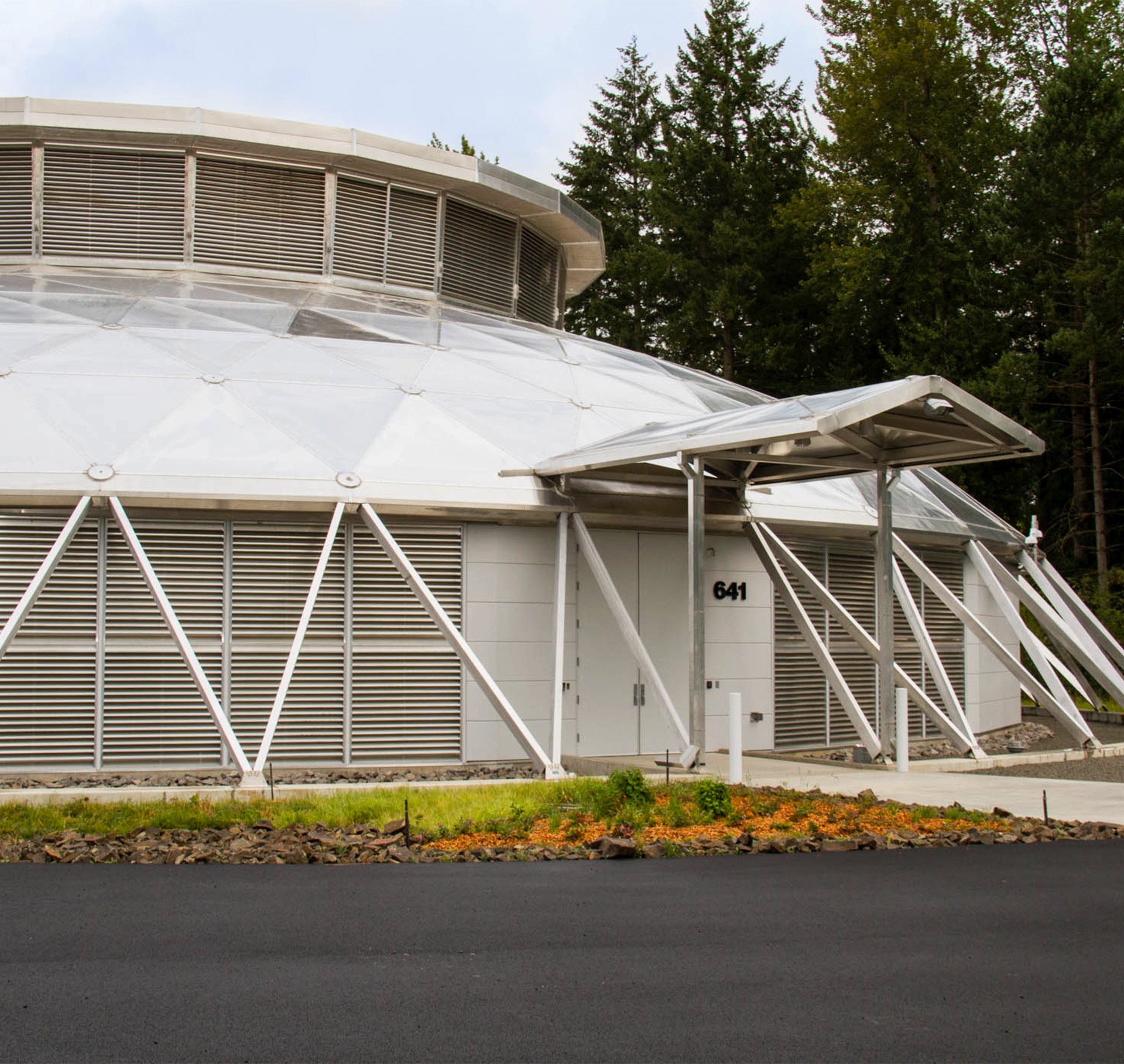 Dome-shaped building with metal supports, entrance marked "641," surrounded by greenery.