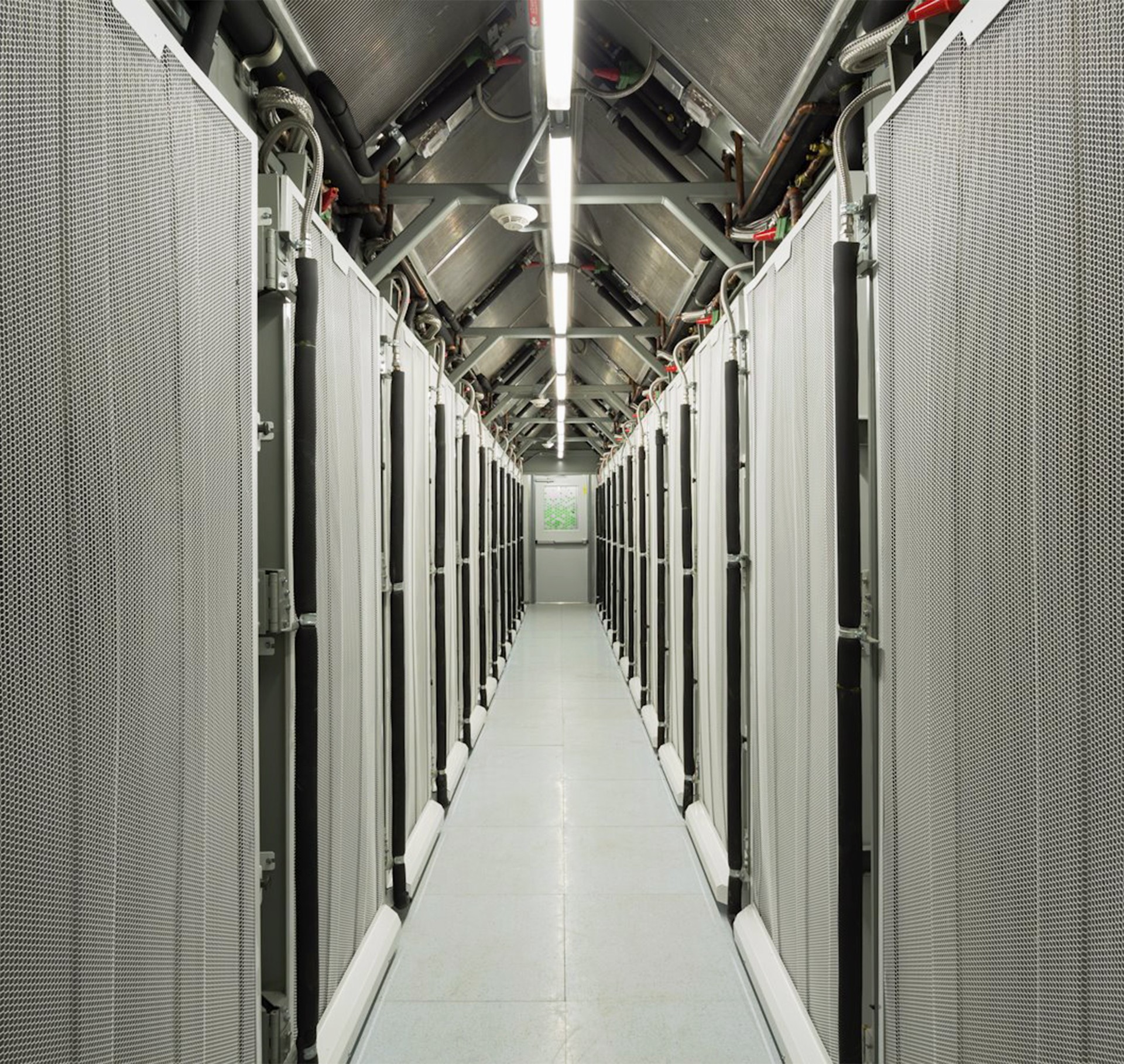 Data center aisle with rows of server racks and overhead fluorescent lighting.