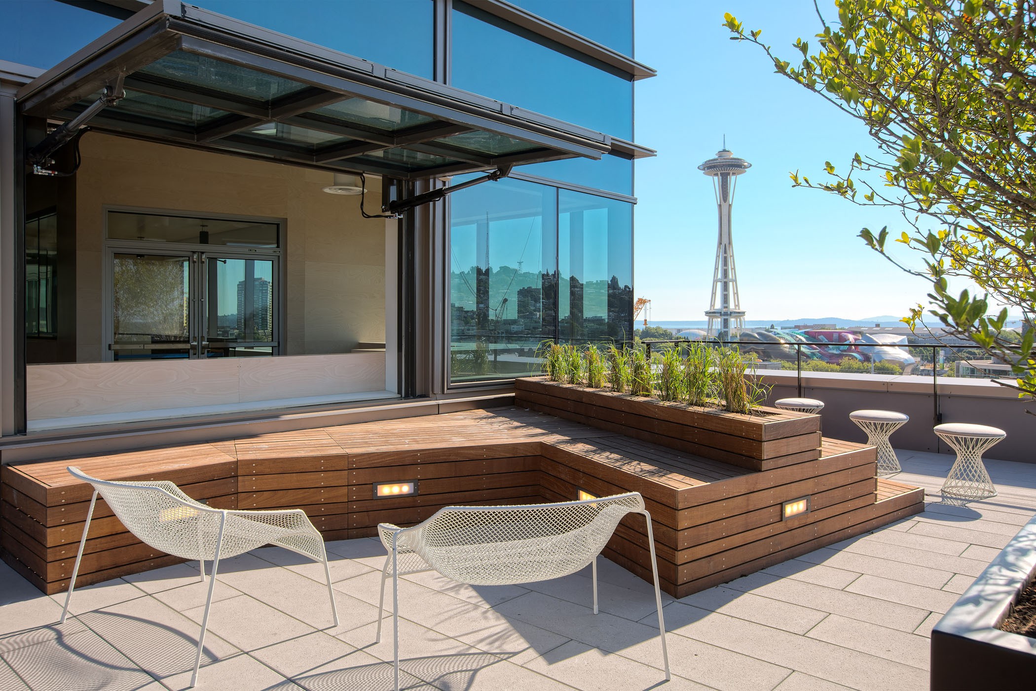 Moderna terraza en la azotea con asientos de madera, sillas de alambre y vista de la Aguja Espacial de Seattle.