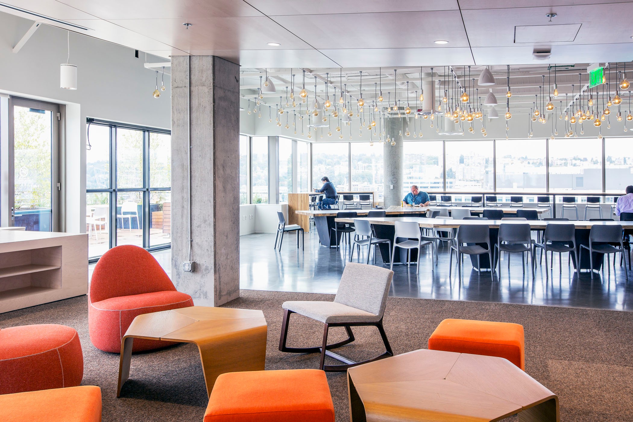 Modern open office space with colorful seating, long tables, and large windows for natural light.