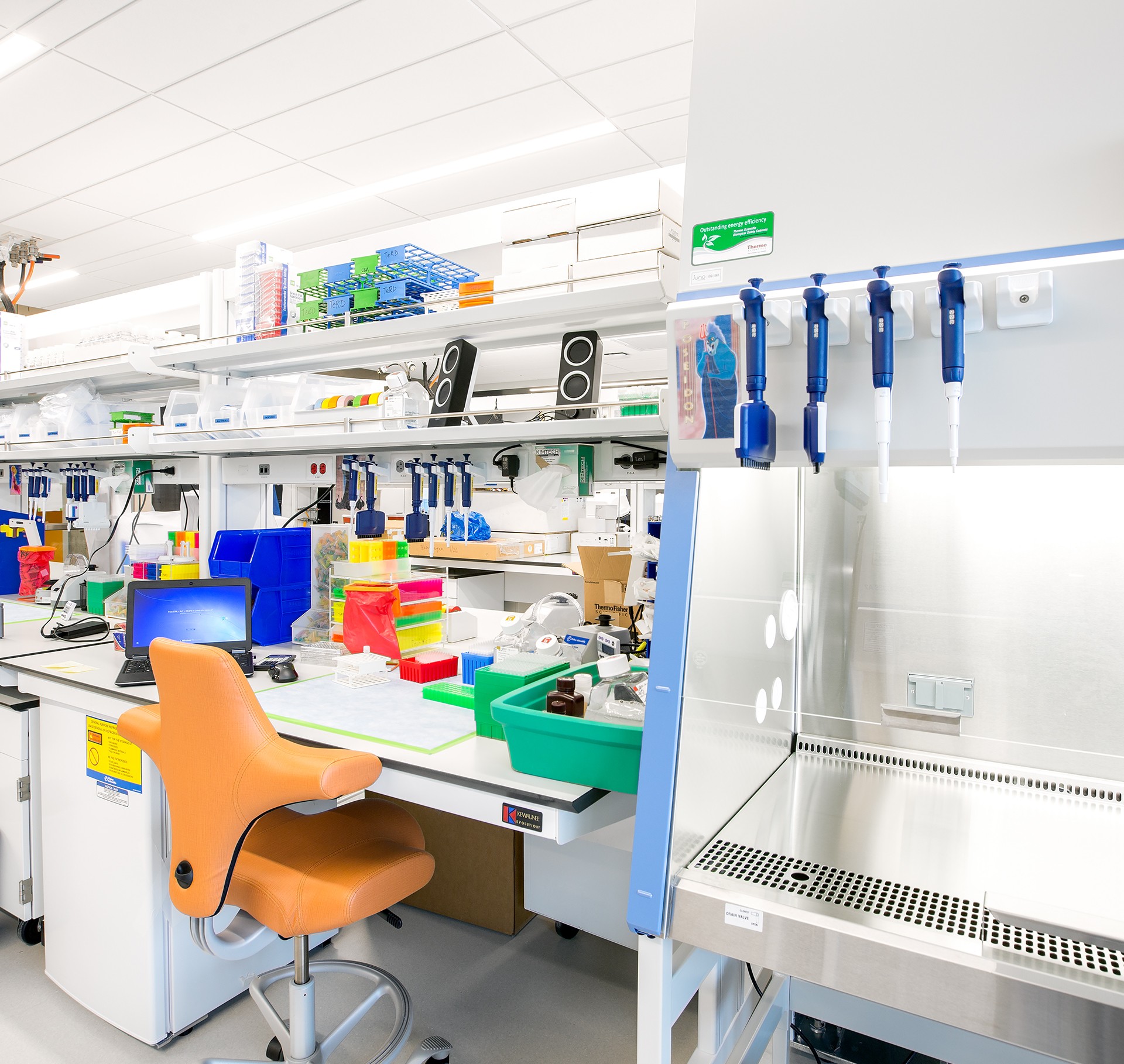 Modern Laboratory Workspace with Equipment and Tools Modern laboratory with equipment, pipettes, orange chair, and a biosafety cabinet.