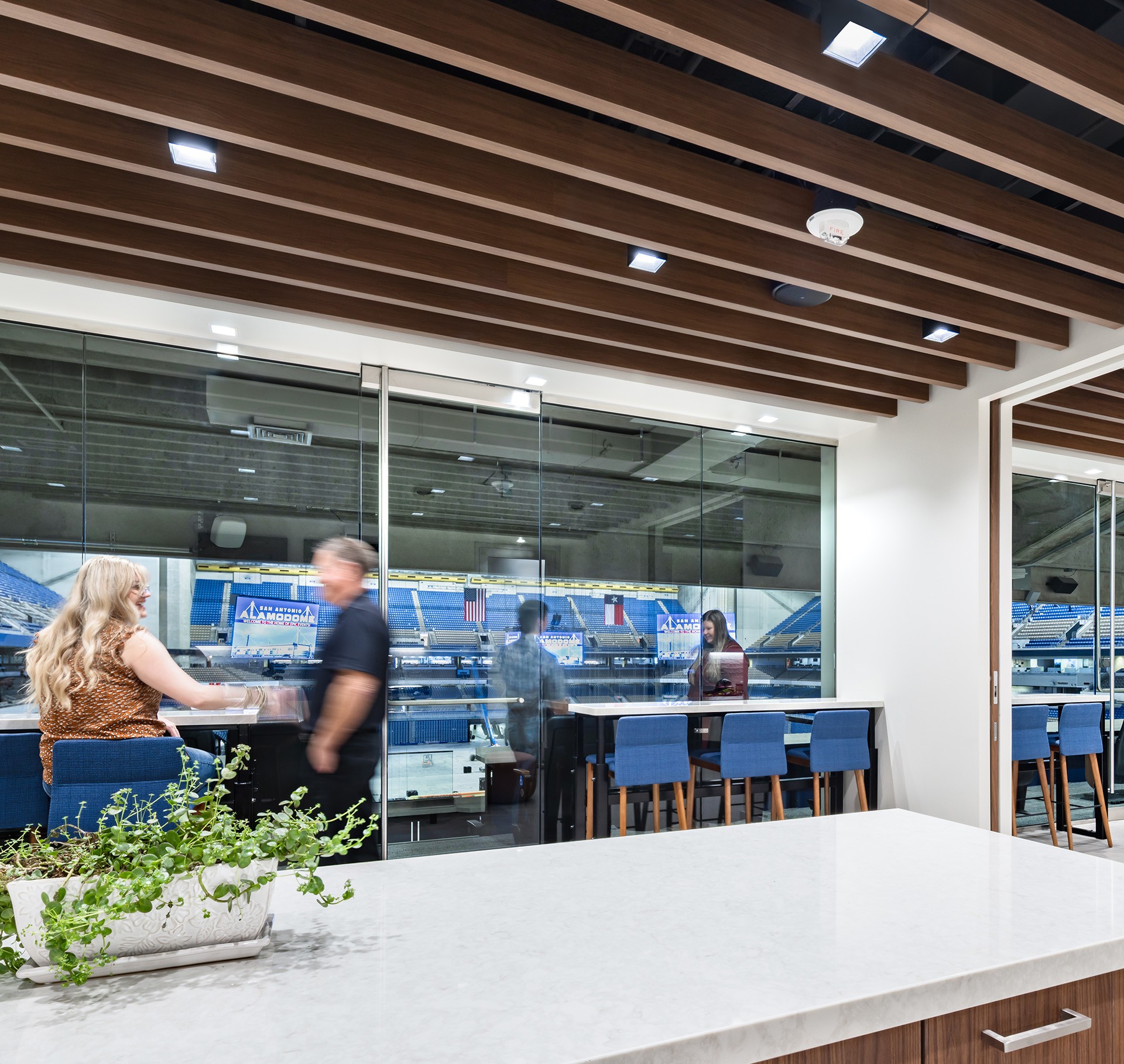 Modern office meeting room with glass walls and stadium view Modern office meeting room with glass walls overlooking a sports stadium and people inside.