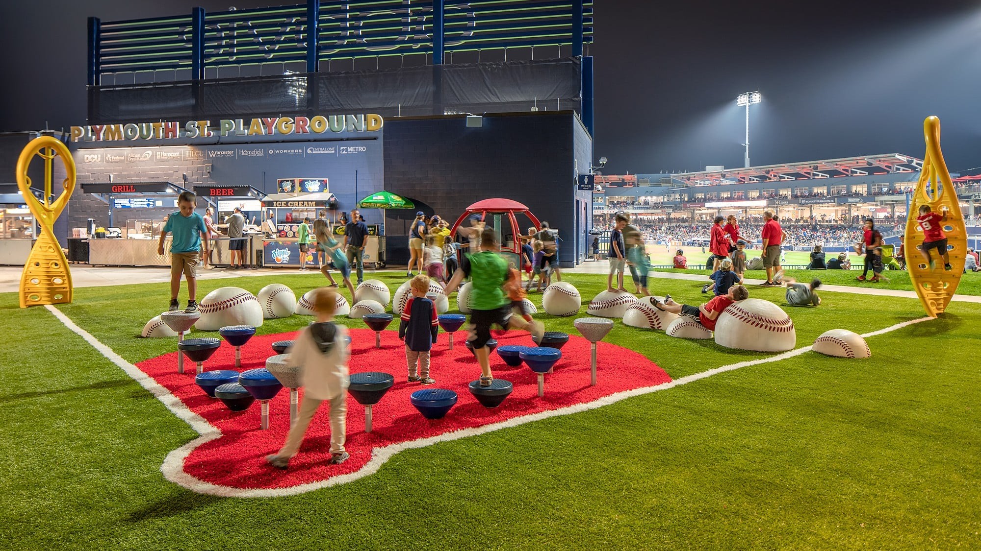Children playing on a baseball-themed playground with oversized baseballs and equipment.