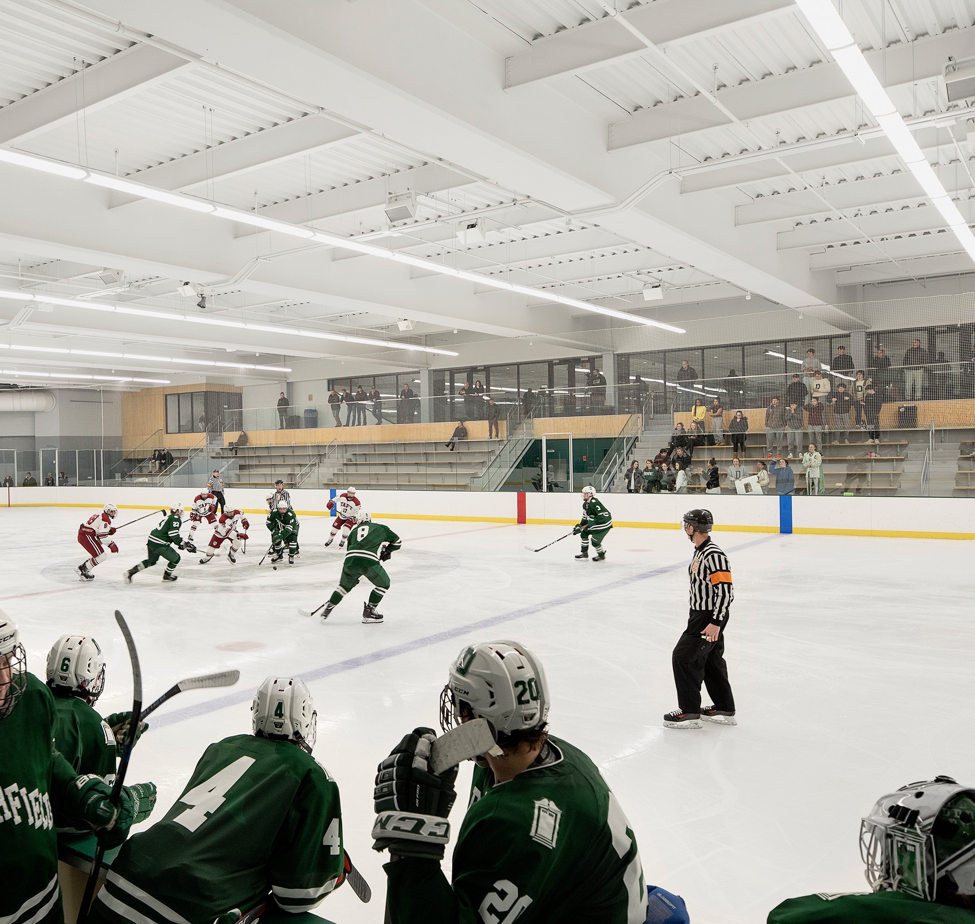 Youth Ice Hockey Game in Indoor Arena with Spectators Ice hockey game in progress with players in green and white jerseys on indoor rink.