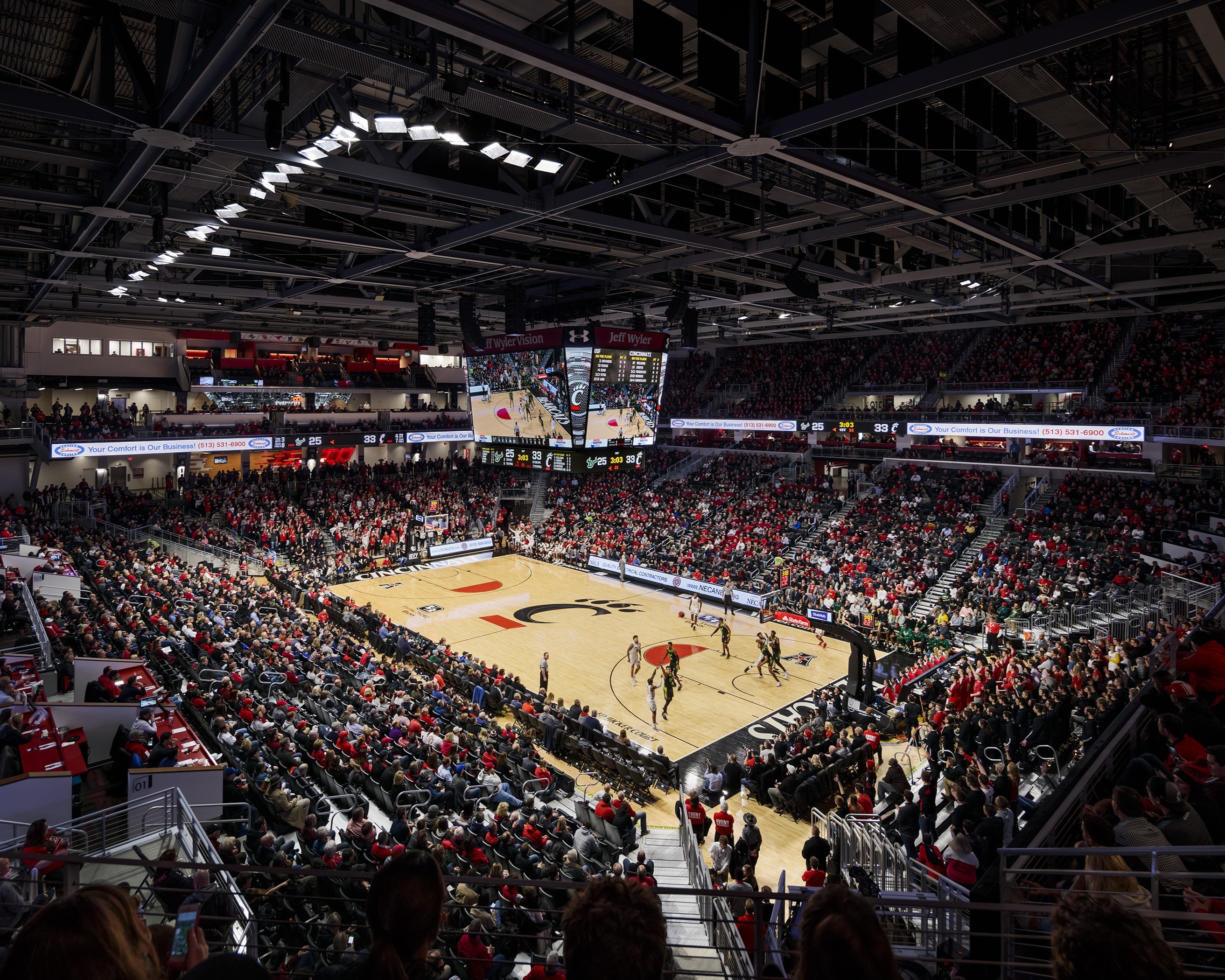 Packed indoor basketball arena during an intense game event Packed indoor basketball arena with players on court and fans in the stands.