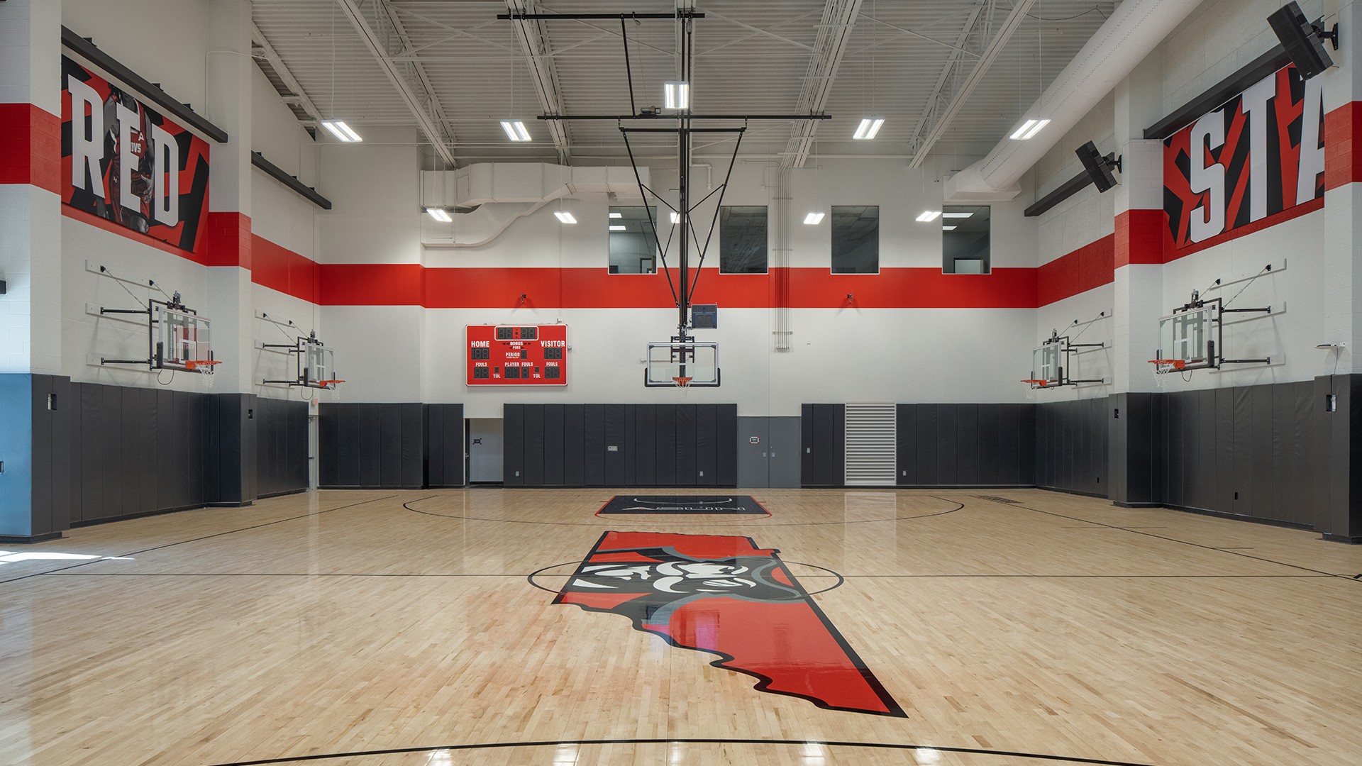 Indoor basketball court with red and black accents and a central state-themed logo.