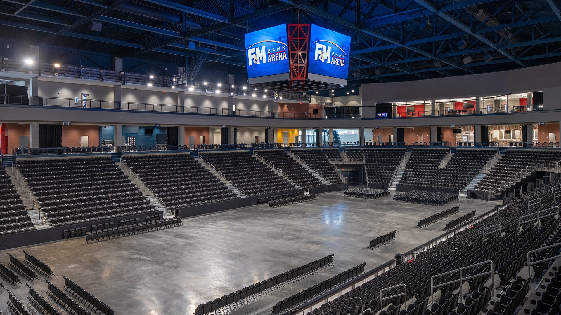Interior view of a modern, empty FM Bank Arena with black seating and large screens.
