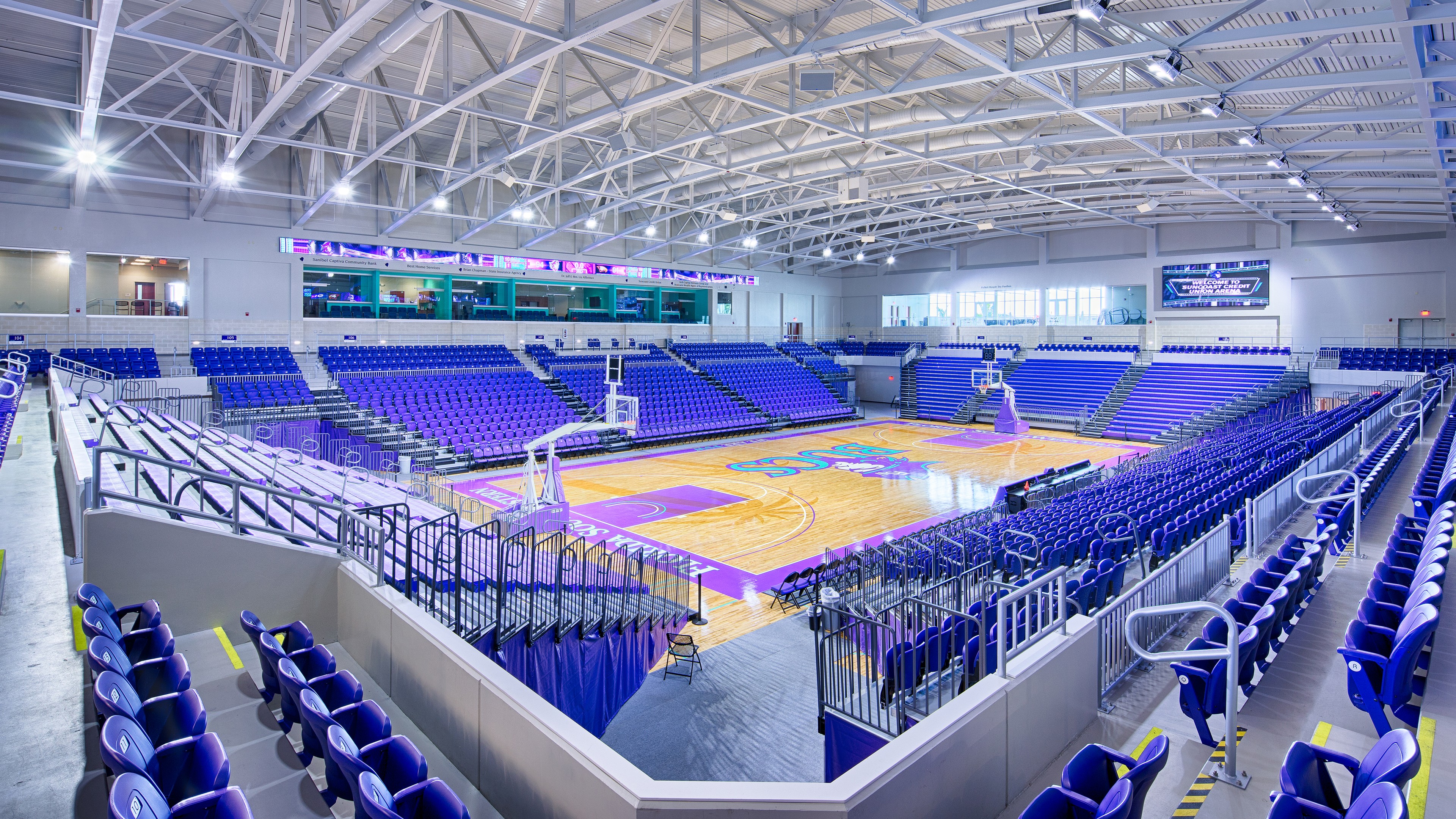 Modern indoor basketball court with purple seating and bright overhead lighting.