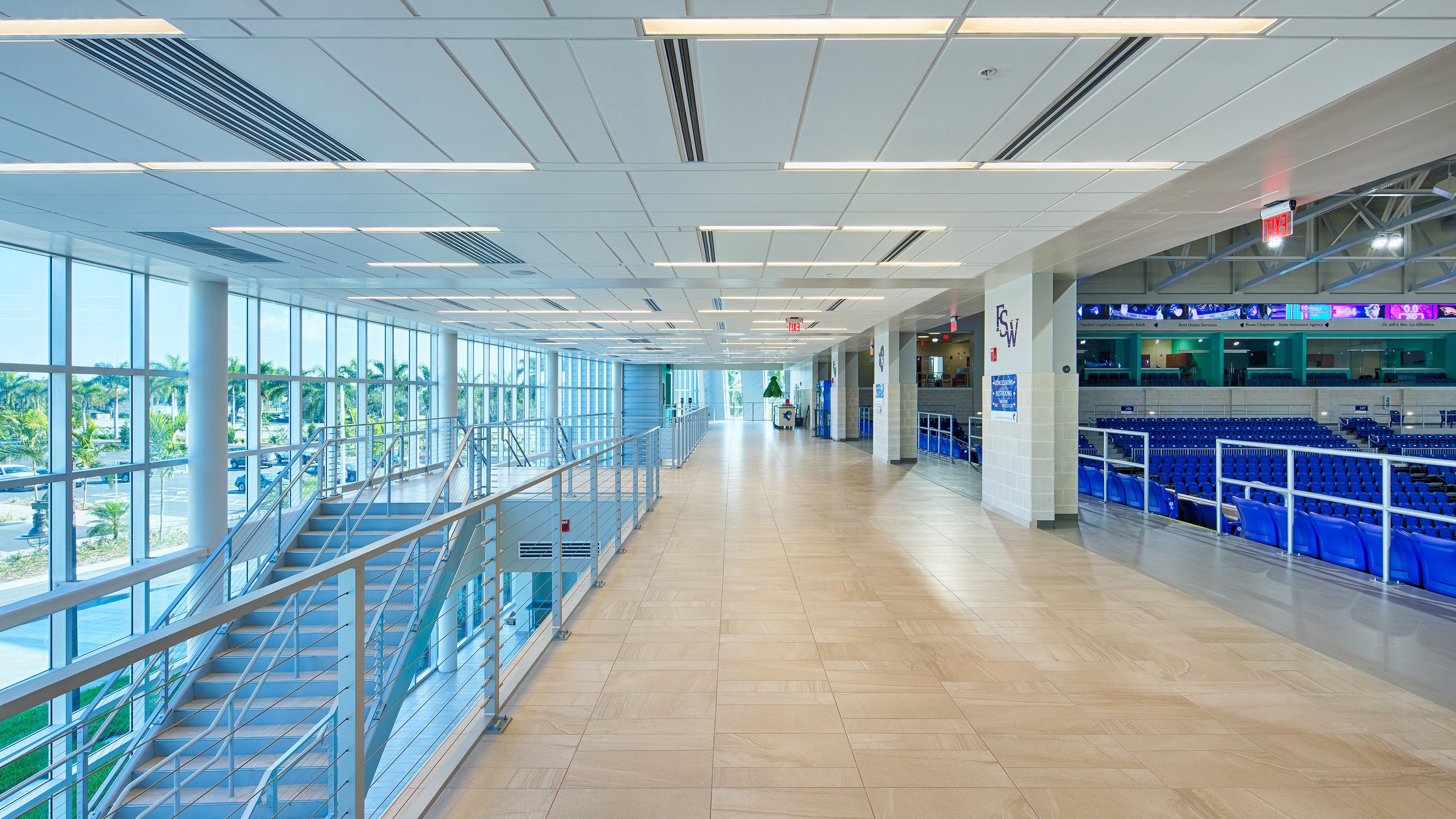 Modern, bright corridor with glass walls and blue seating in a sports arena interior.
