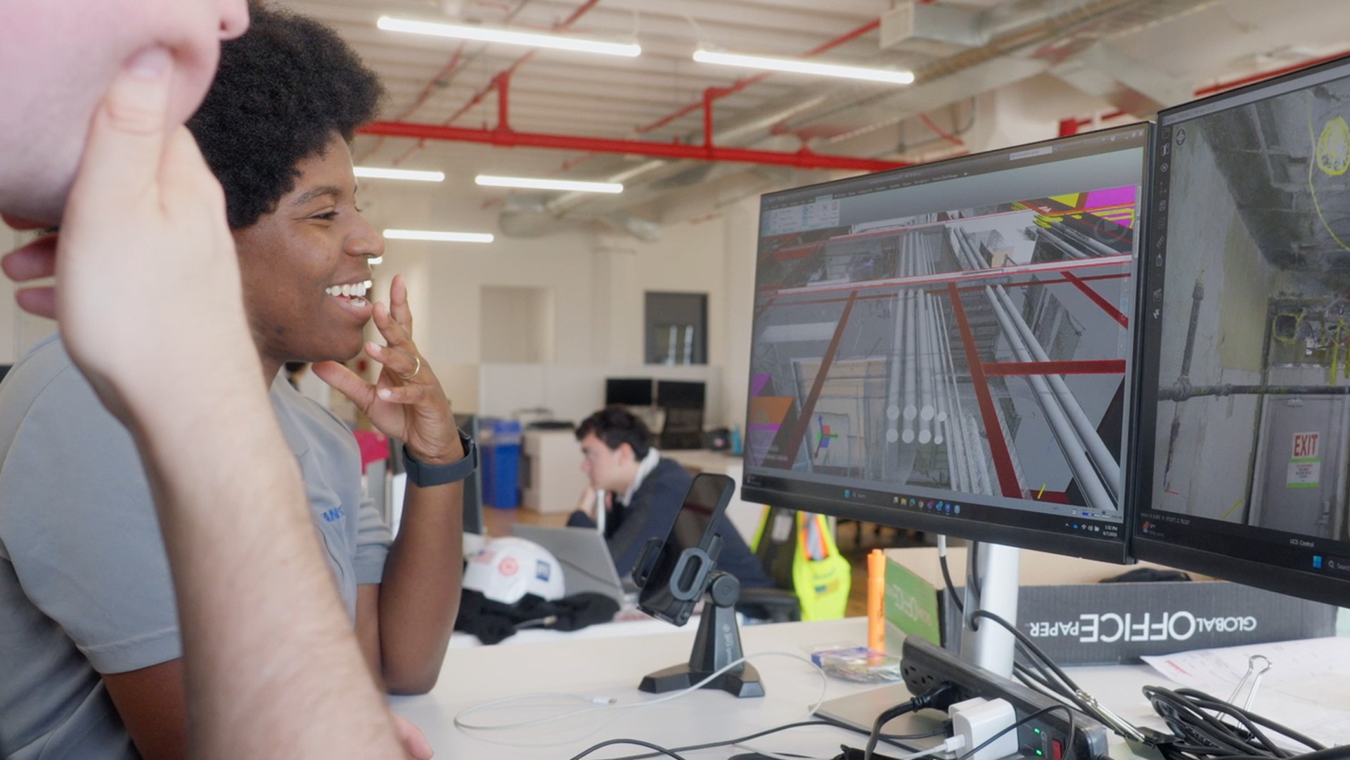 Two professionals analyzing 3D architectural models on dual monitors in an office.