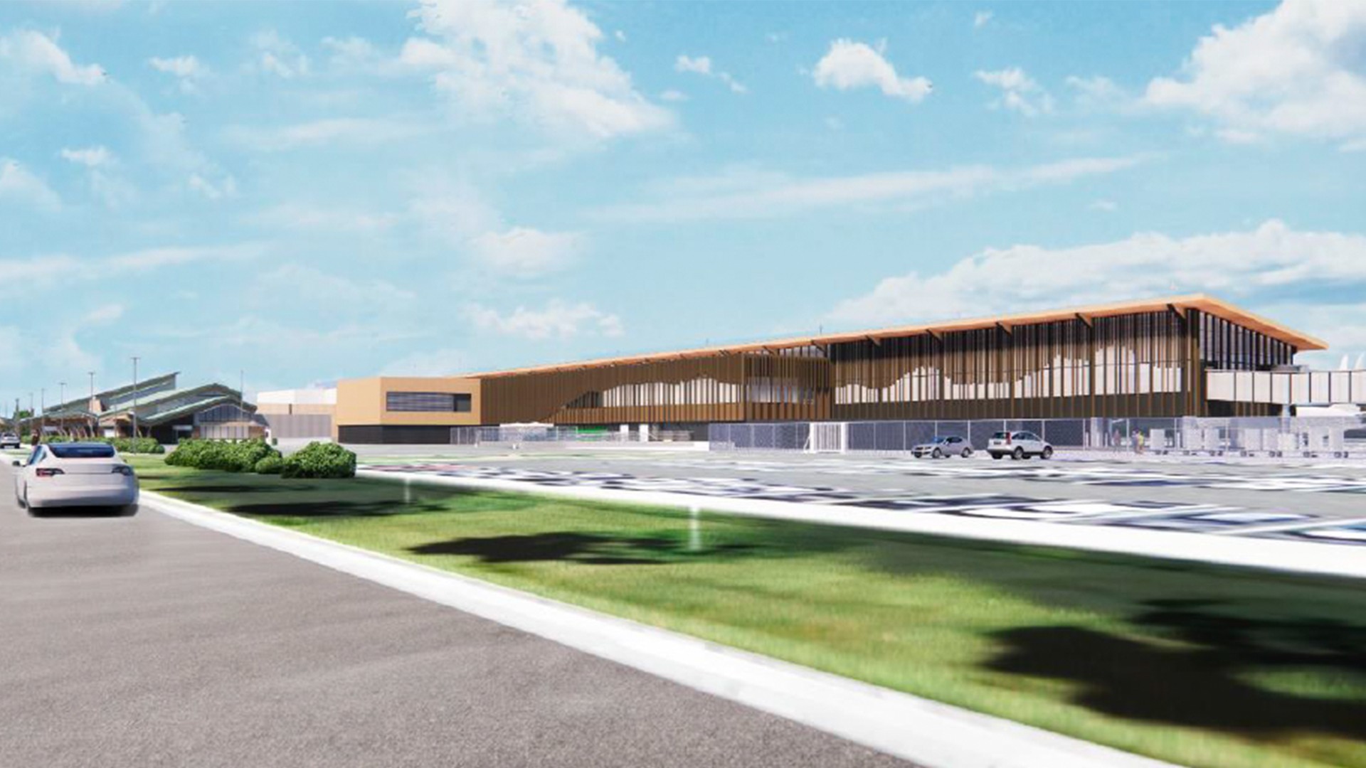 Modern airport terminal with large glass windows and adjacent parking area under blue sky.