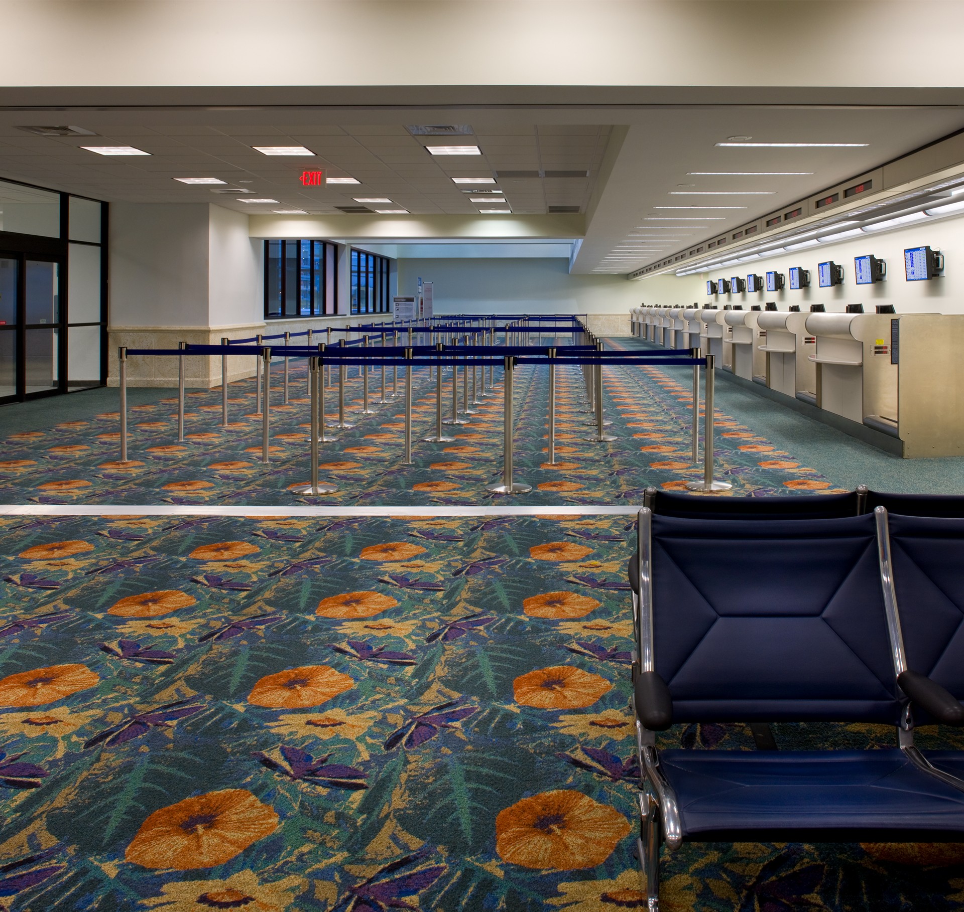 Empty airport check-in area with colorful floral carpet and blue seating.