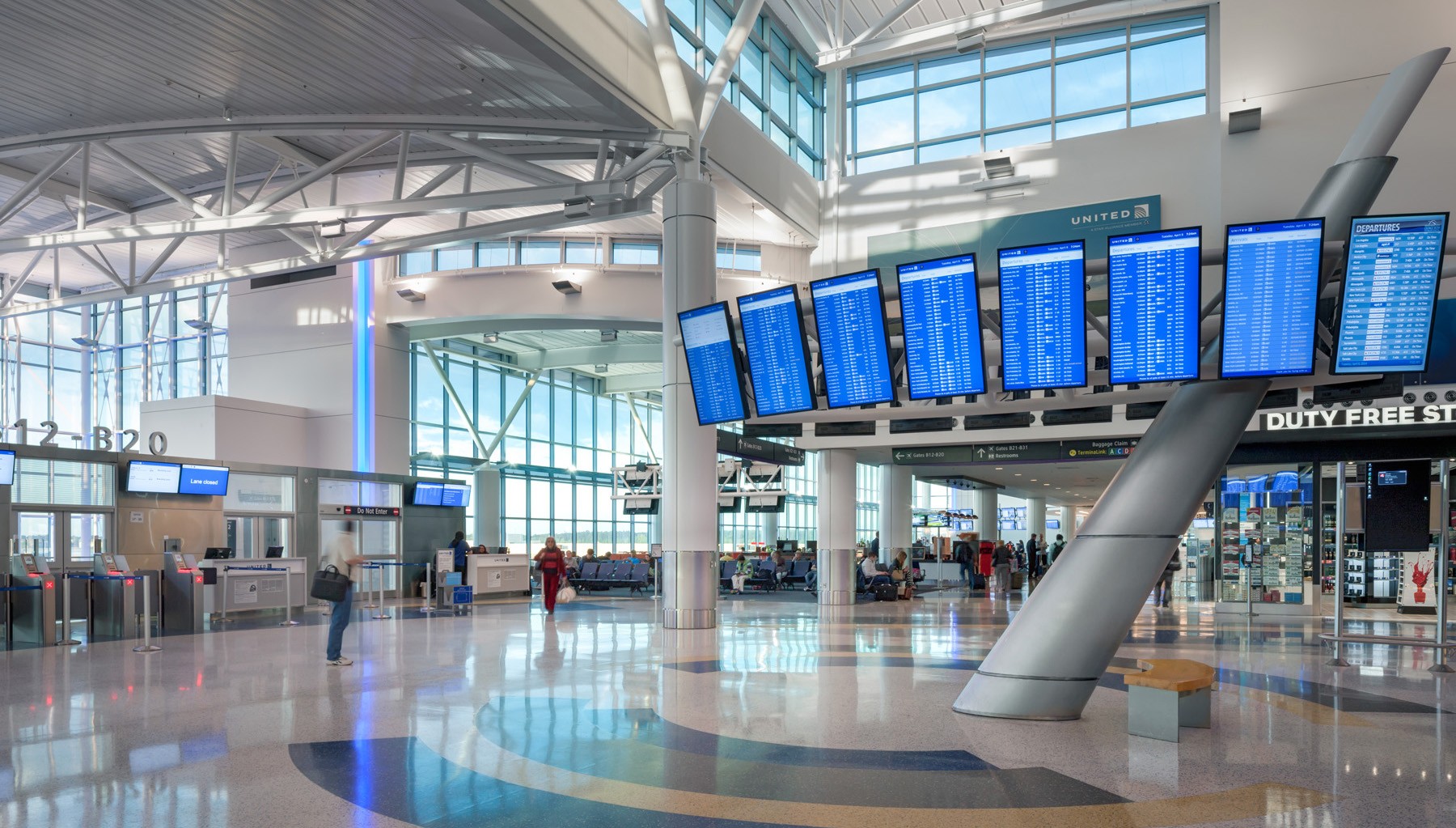 Modern airport terminal with flight information screens, ticket counters, and a duty-free store.