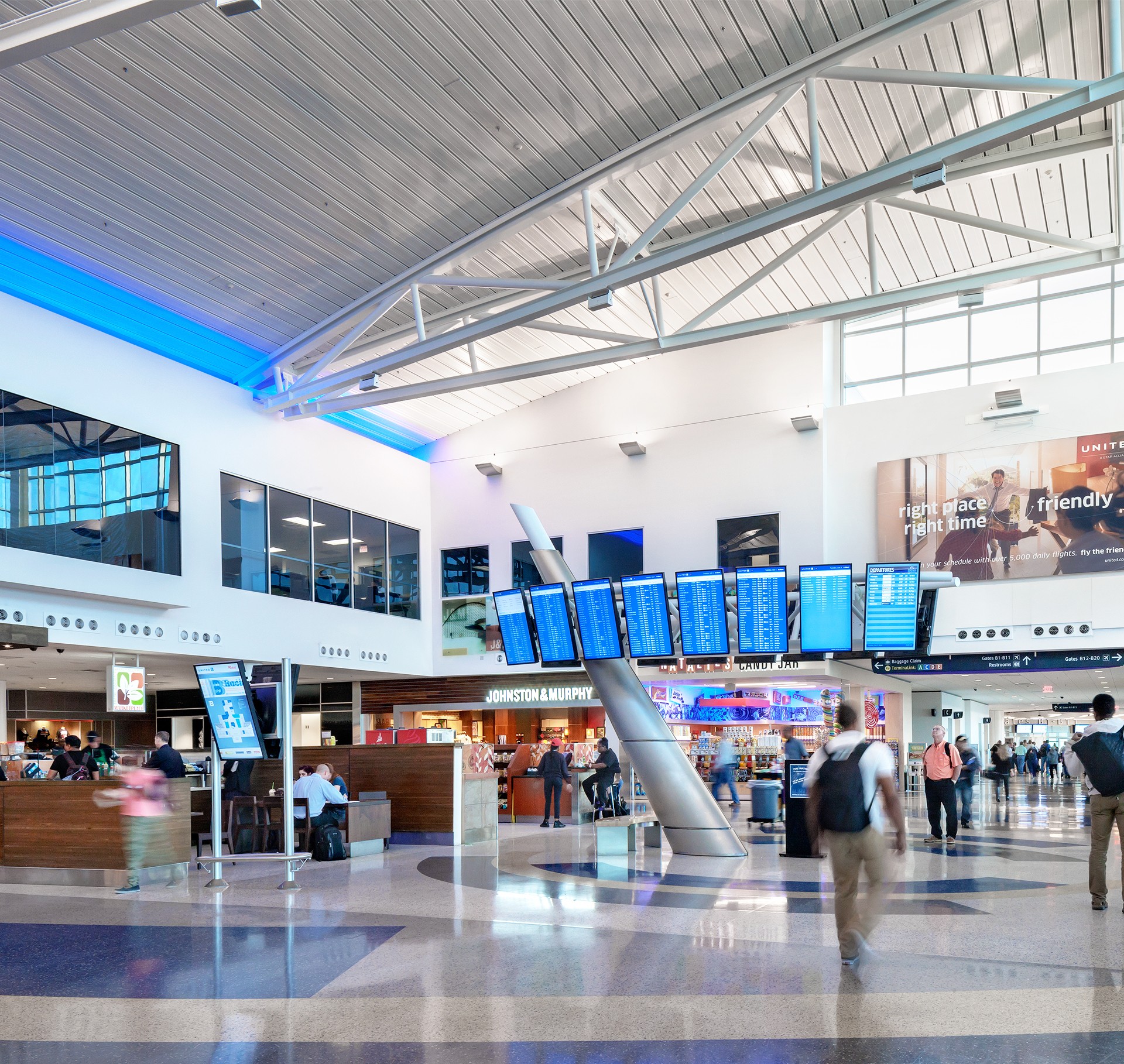 Modern airport terminal with flight information displays A bustling airport terminal with digital flight displays, shops, and travelers walking by.
