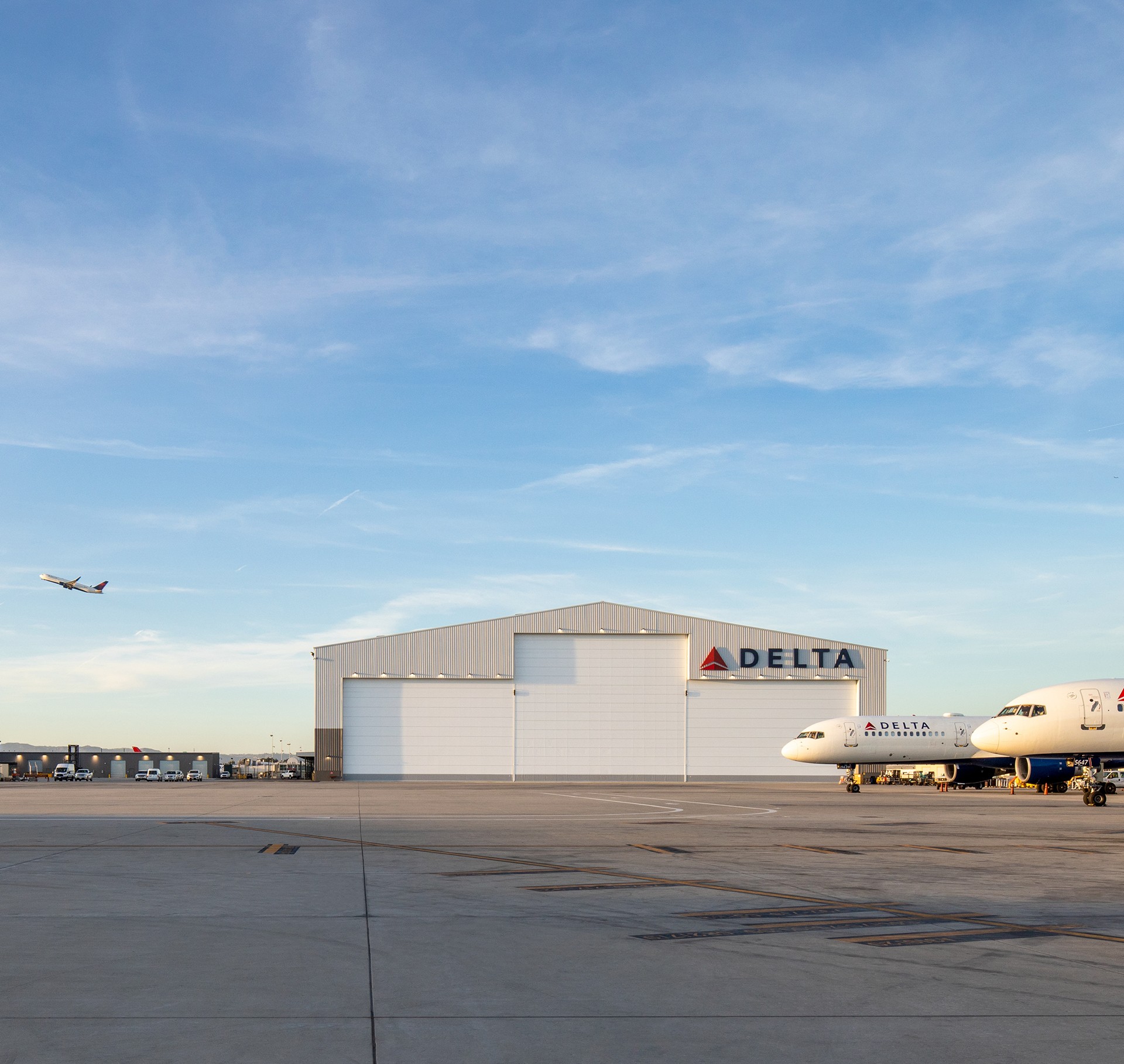 Delta Airlines hangar with planes on airport runway at sunset Delta Airlines planes parked near a large hangar under a clear blue sky at the airport.