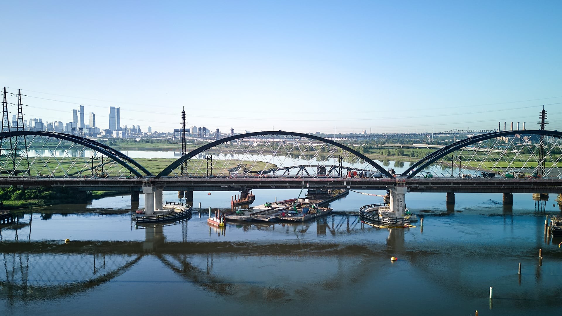 Modern Steel Bridge Over Calm River with City Skyline View Steel arch bridge over calm river with city skyline and clear blue sky in background.