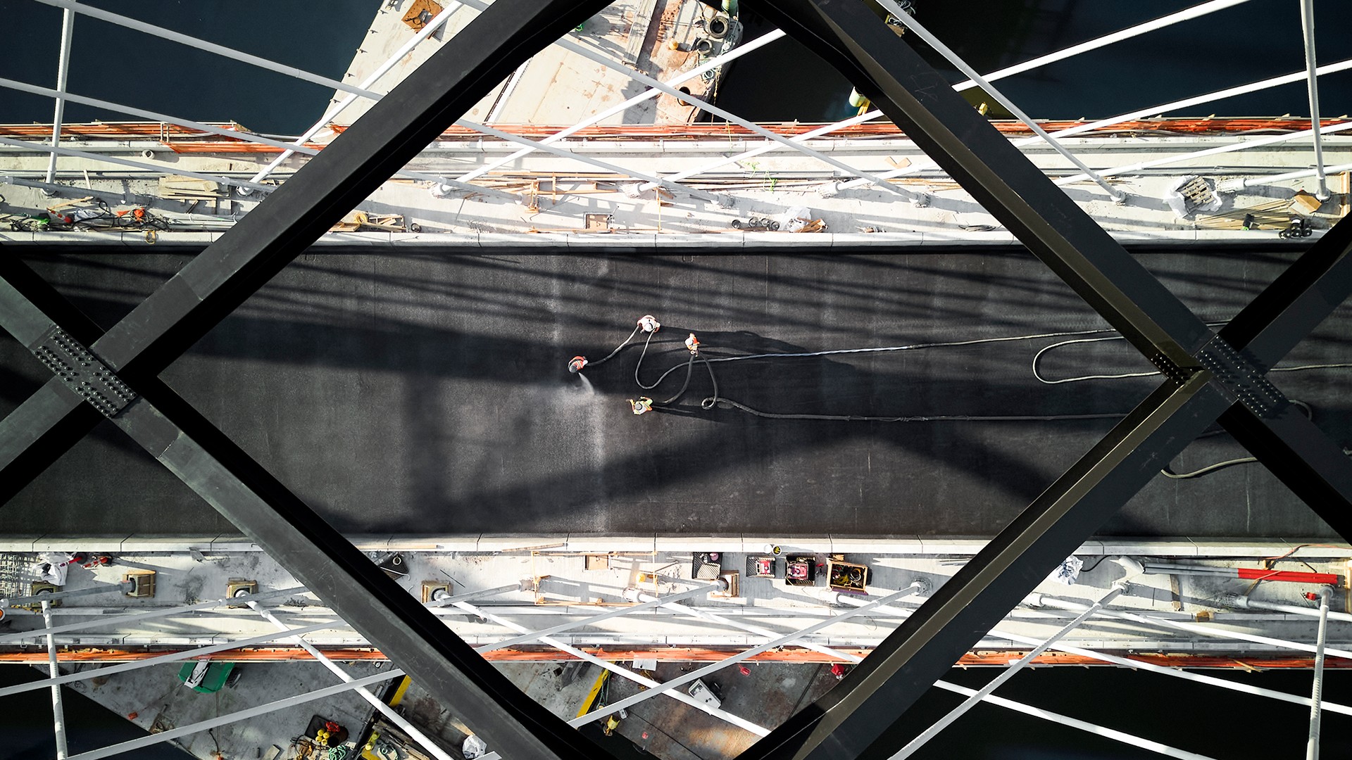 Aerial view of workers on a large ship's deck with shadows Aerial view of workers on a bridge under construction with steel beams and cables.