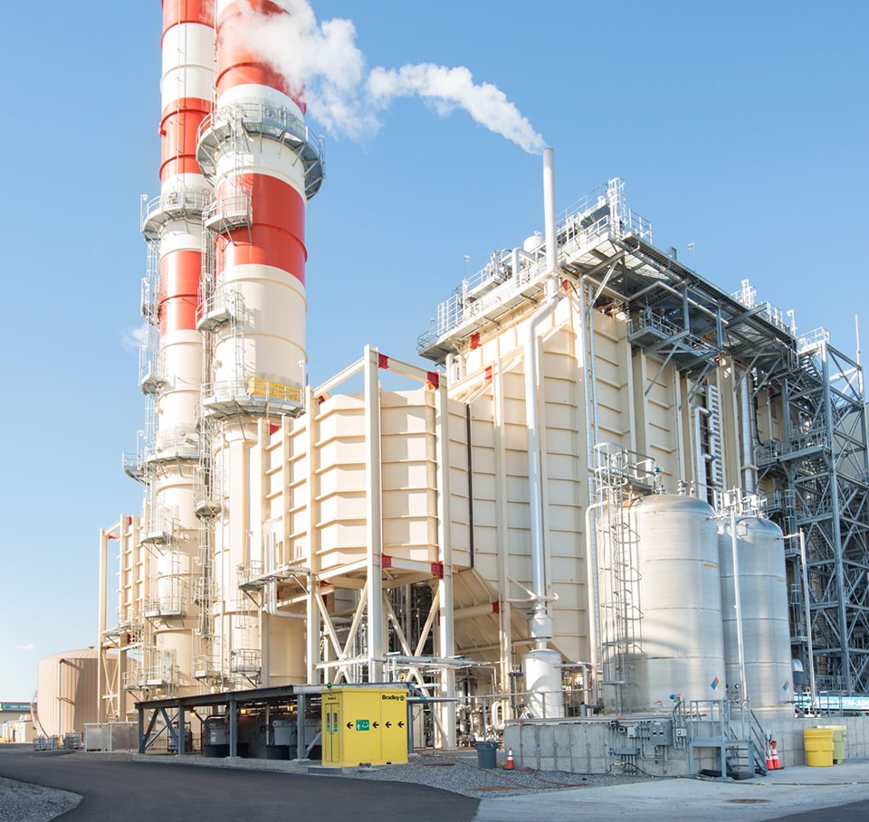 Industrial power plant with tall red and white smokestacks emitting white smoke.
