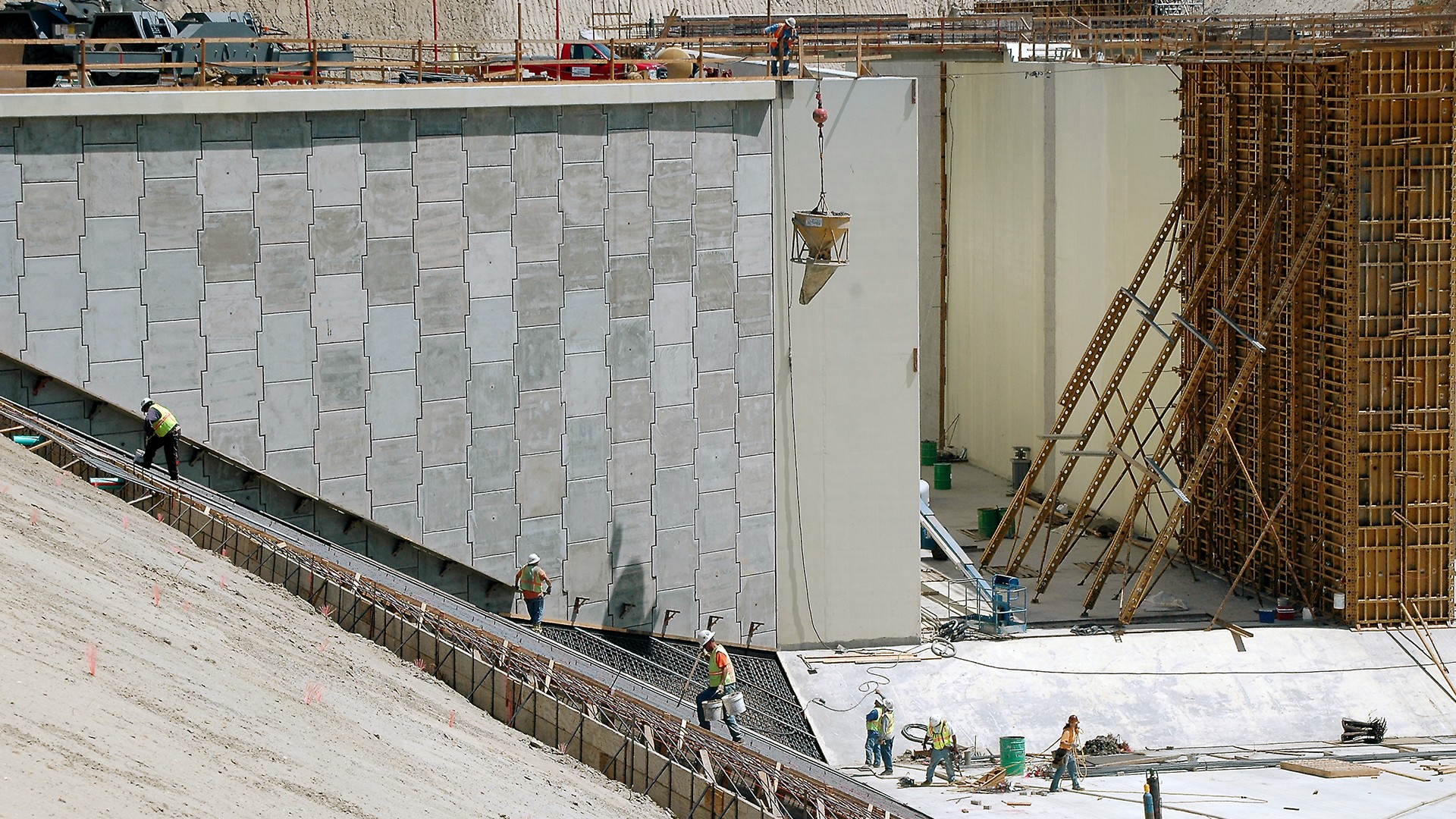 Construction workers building a large concrete structure with scaffolding and cranes.