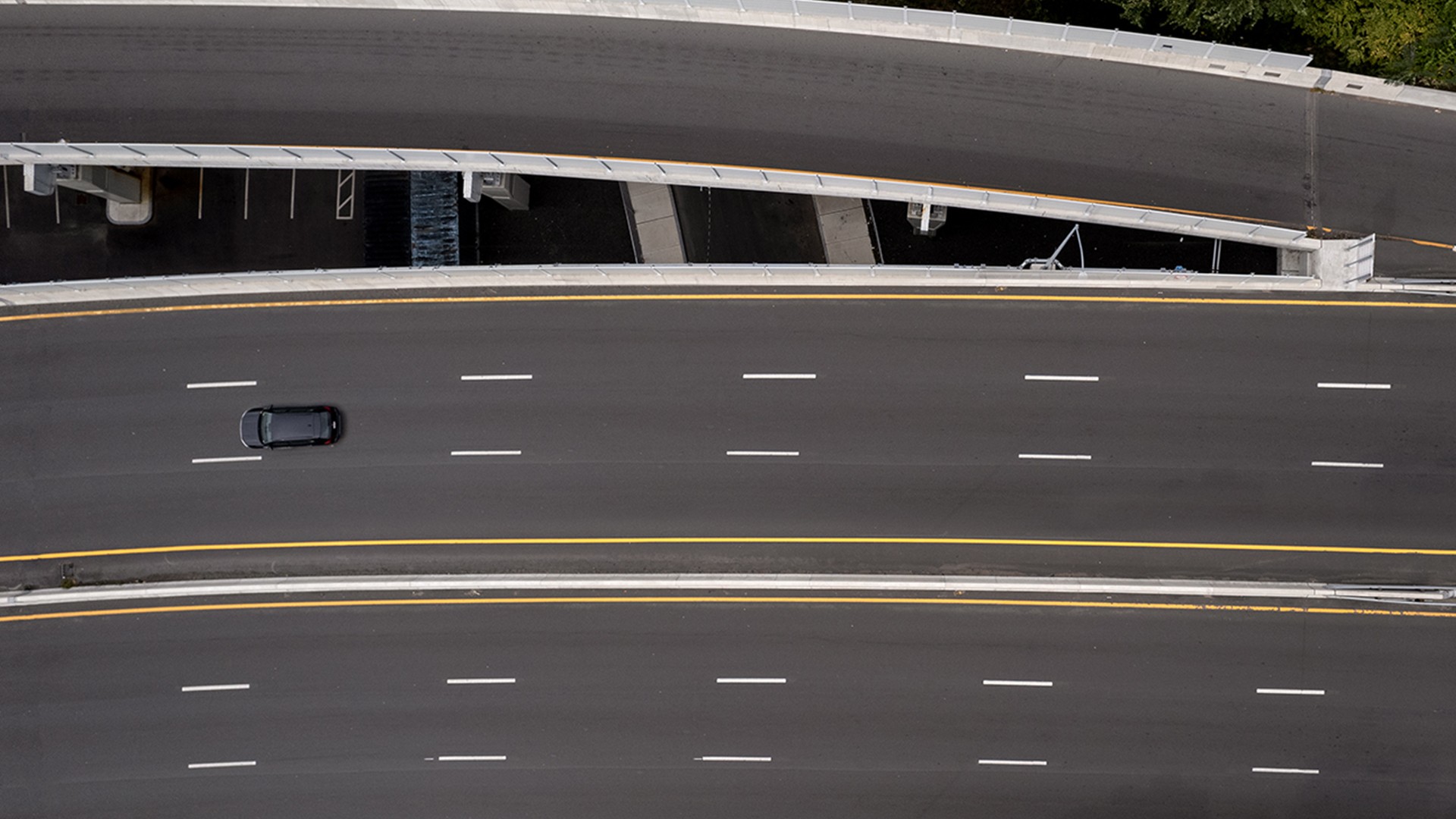 Aerial view of an empty multi-lane highway with a single black car driving on it.