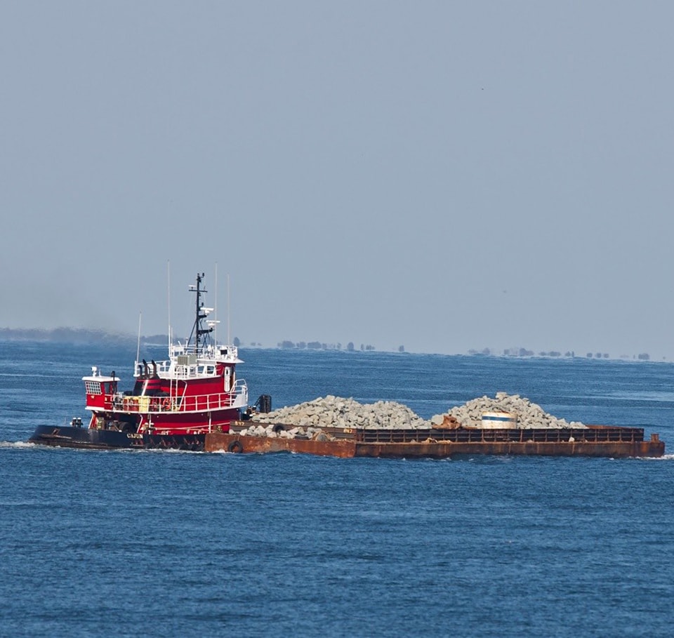 Tugboat Hauling Barge Loaded with Rocks on Calm Blue Water Tugboat towing a barge loaded with rocks on calm blue ocean water under clear sky.