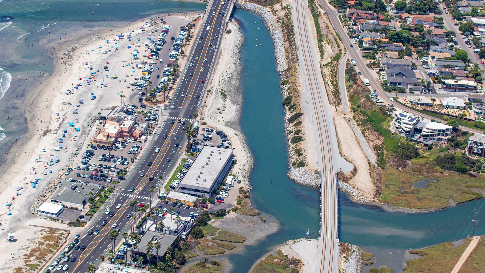 Aerial view of a coastal highway with beach, ocean, and residential area alongside.