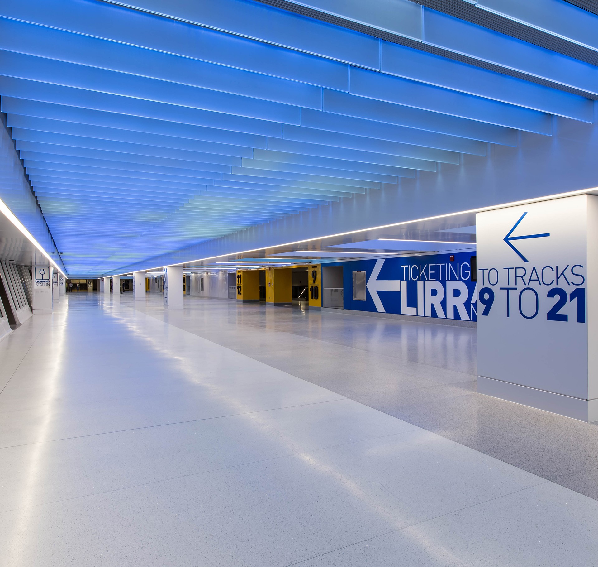 Modern train station corridor with blue illuminated ceiling Modern train station corridor with blue ceiling lights and directional signs for tracks.