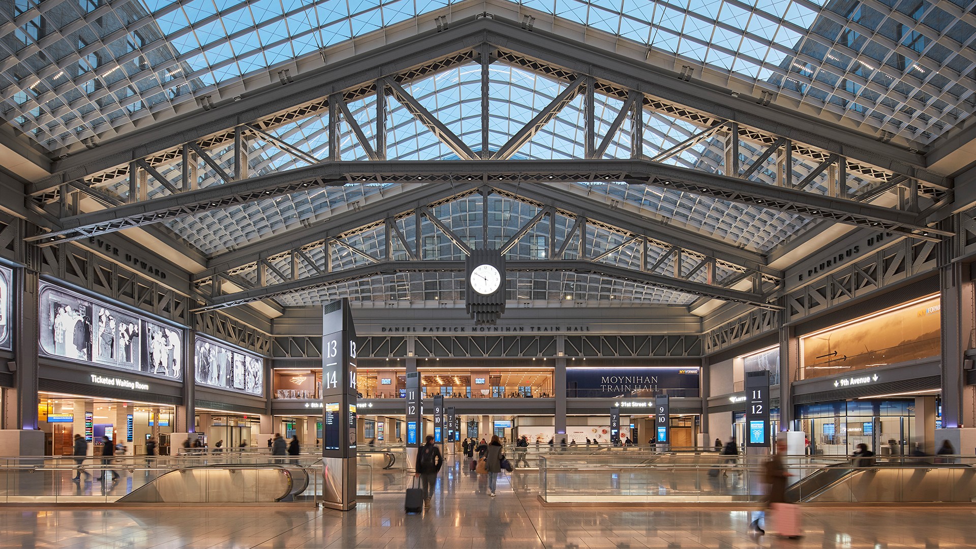 Interior view of a modern train station hall with glass ceiling and travelers.