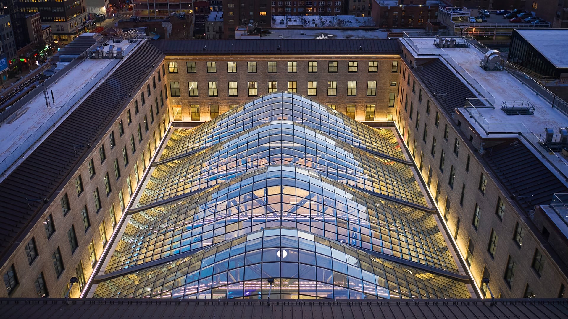 Aerial view of a modern glass roof structure inside a historic building courtyard at dusk.