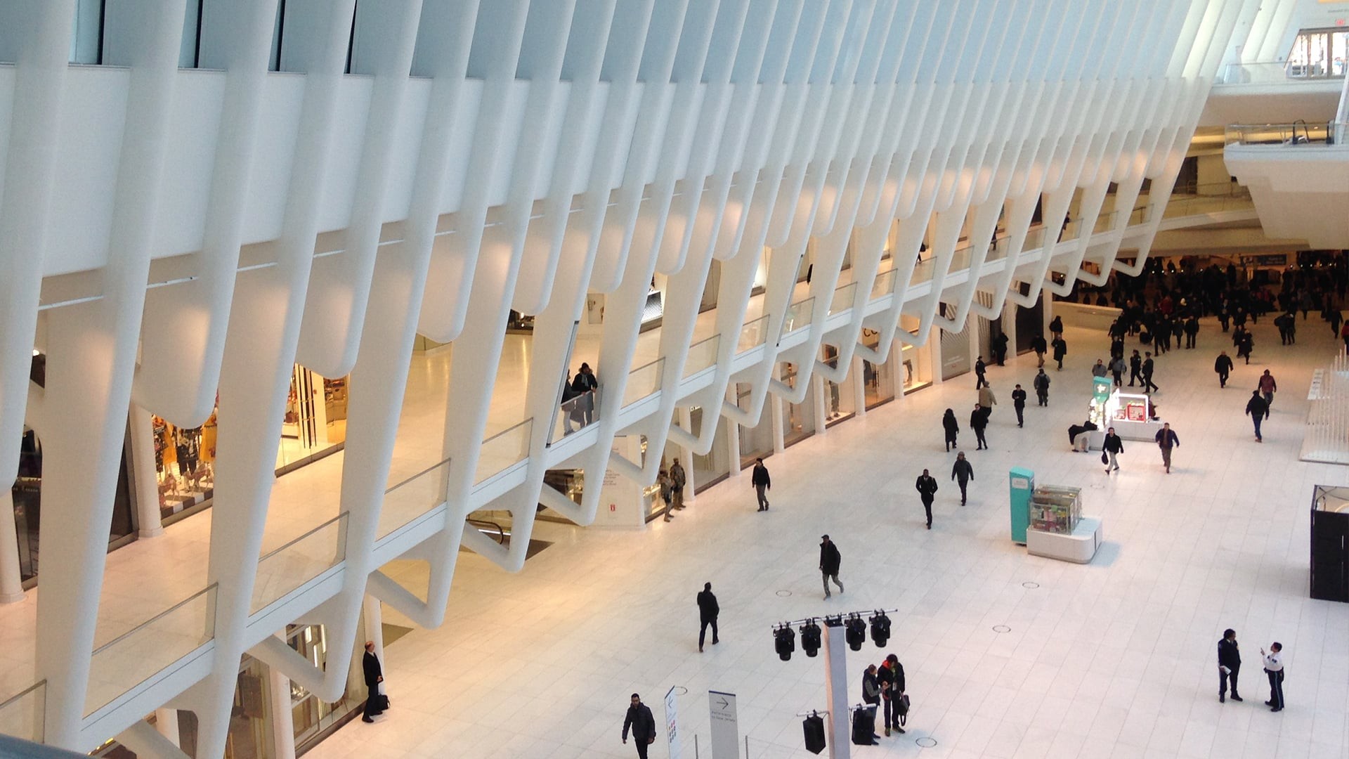 Interior view of a modern shopping mall with white architectural beams and shoppers.