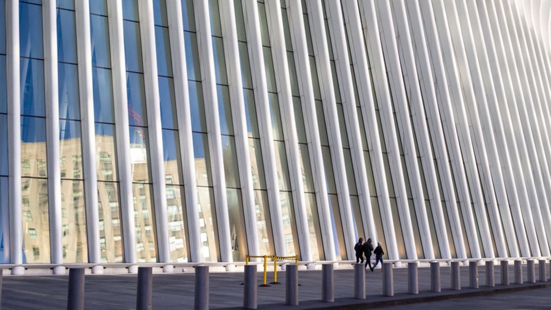 Modern architectural structure with tall vertical beams and people walking nearby.