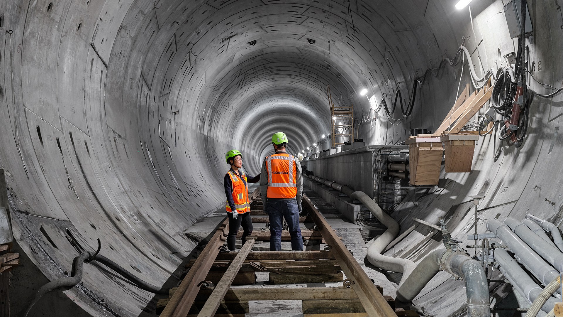 Two construction workers in safety gear inspecting railway tracks inside a tunnel.