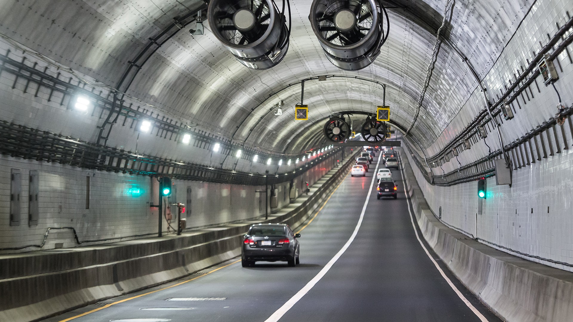 Cars Driving Through Well-Lit Urban Tunnel with Ventilation Fans Cars driving through a well-lit tunnel with ventilation fans and traffic signals.