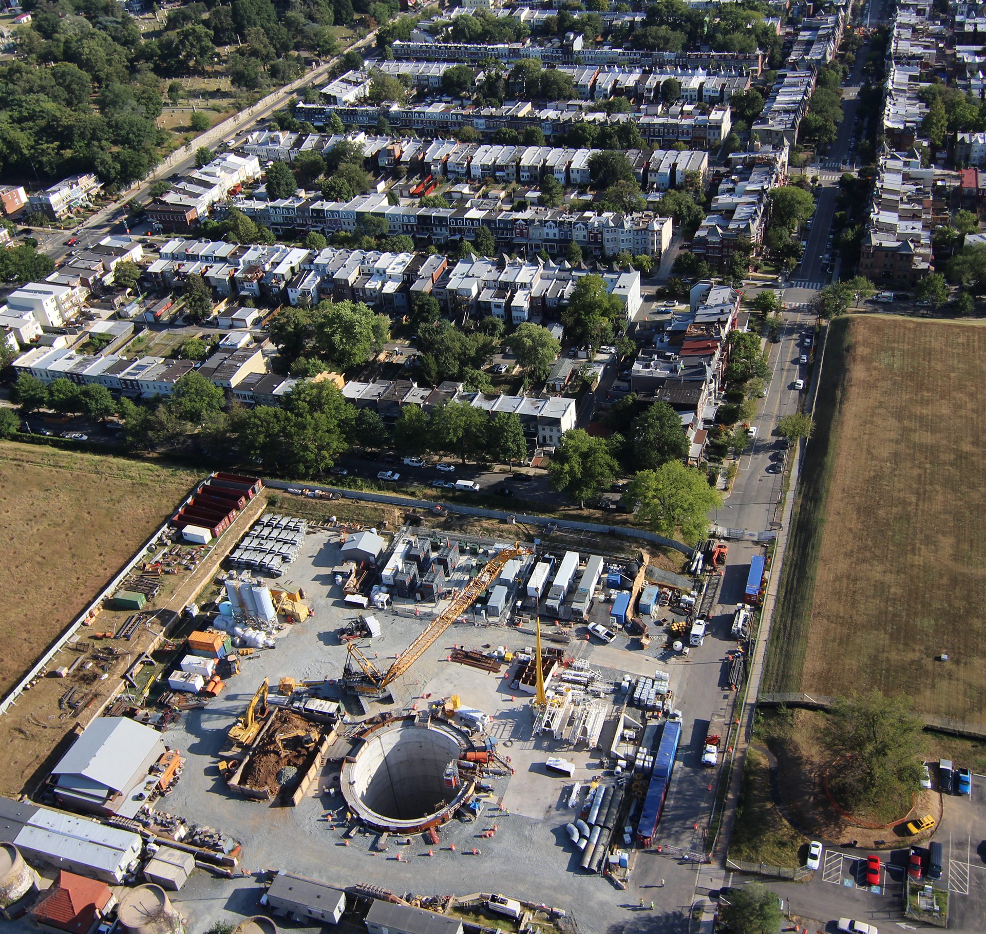 Aerial view of urban construction site with cranes and residential neighborhood nearby.