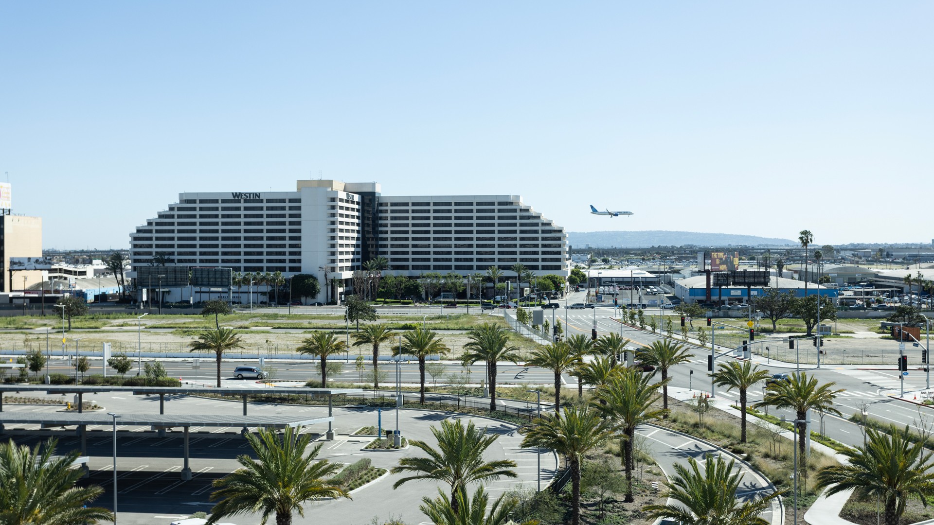 Westin Hotel Near Airport with Palm Trees and Clear Sky Westin hotel near an airport runway with a plane landing and palm trees in foreground.