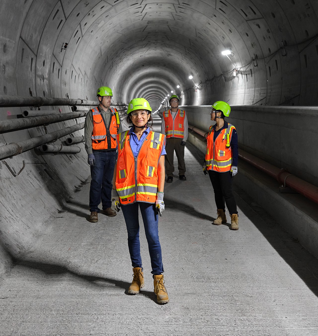 Construction workers inspecting tunnel with safety gear on site Construction workers wearing safety gear and helmets inside a tunnel under construction.