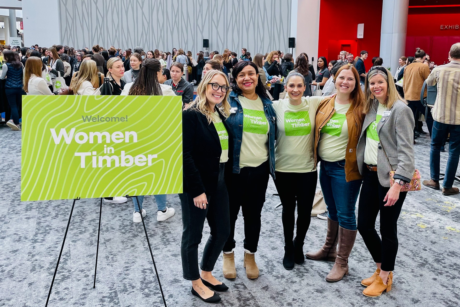 Group of women wearing "Women in Timber" shirts at a timber industry event with crowd.