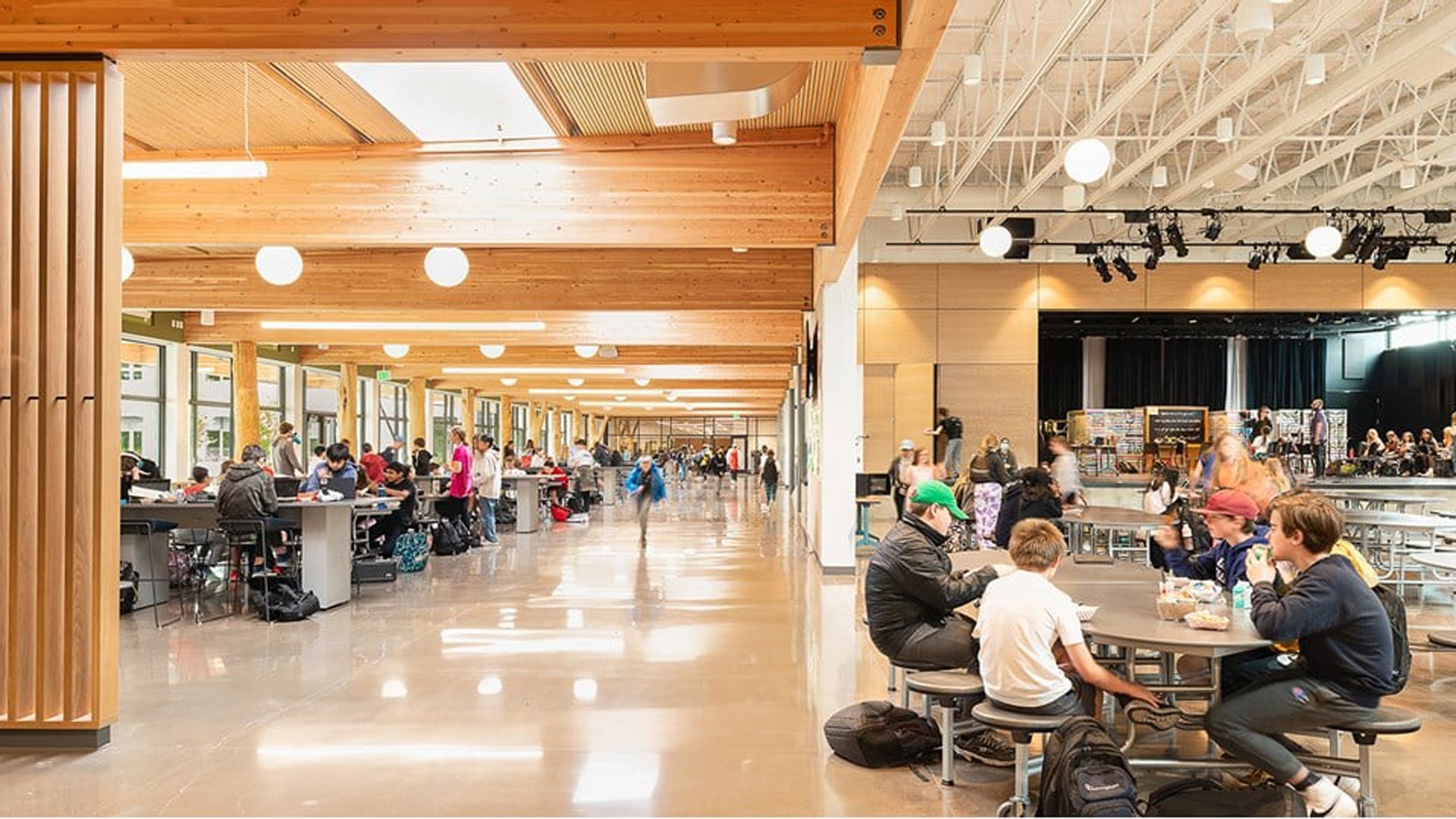 Spacious school cafeteria with students eating and socializing at round tables.