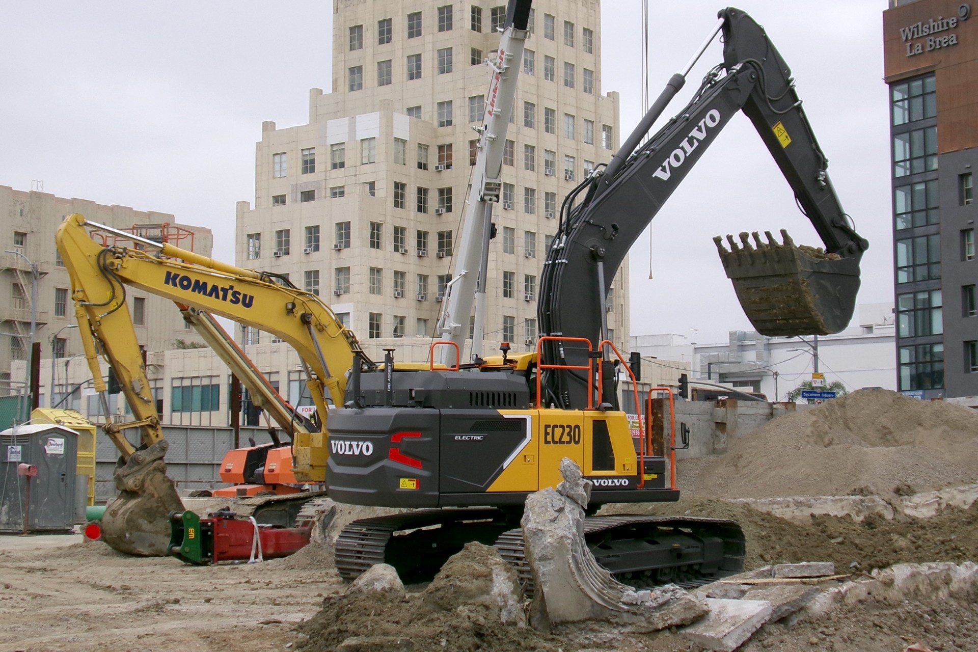 Volvo and Komatsu Excavators at Urban Construction Site Volvo and Komatsu excavators at an urban construction site with buildings in the background.